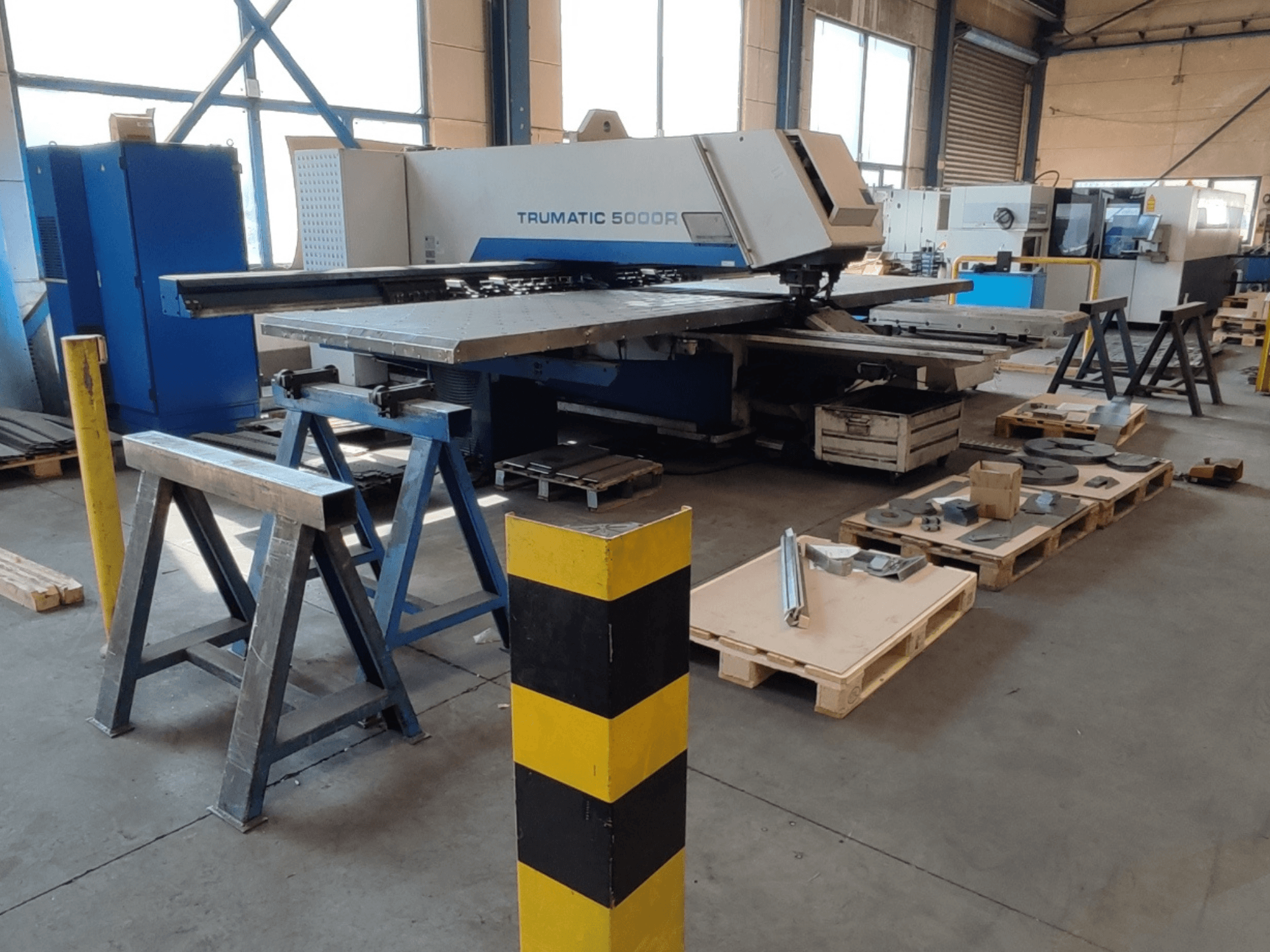 TRUMPF Trumatic 5000 R CNC stroj za probijanje u radionici, bočni pogled s alatima i materijalima na paletama u blizini.