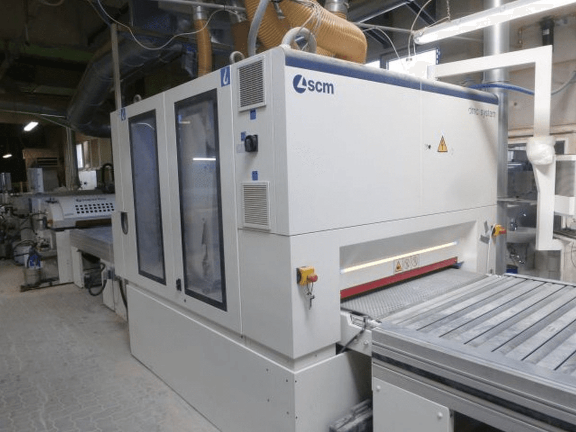 Tračna brusilica SCM DMC SY TC 1350 u radionici, bočni pogled koji prikazuje upravljačku ploču i brusnu površinu sa sigurnosnim značajkama.