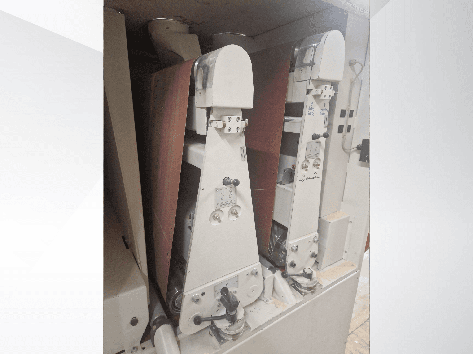 Dva industrijska stroja za brušenje s crvenim brusnim trakama, prednji pogled, s prikazom kontrola i metalnih komponenti.