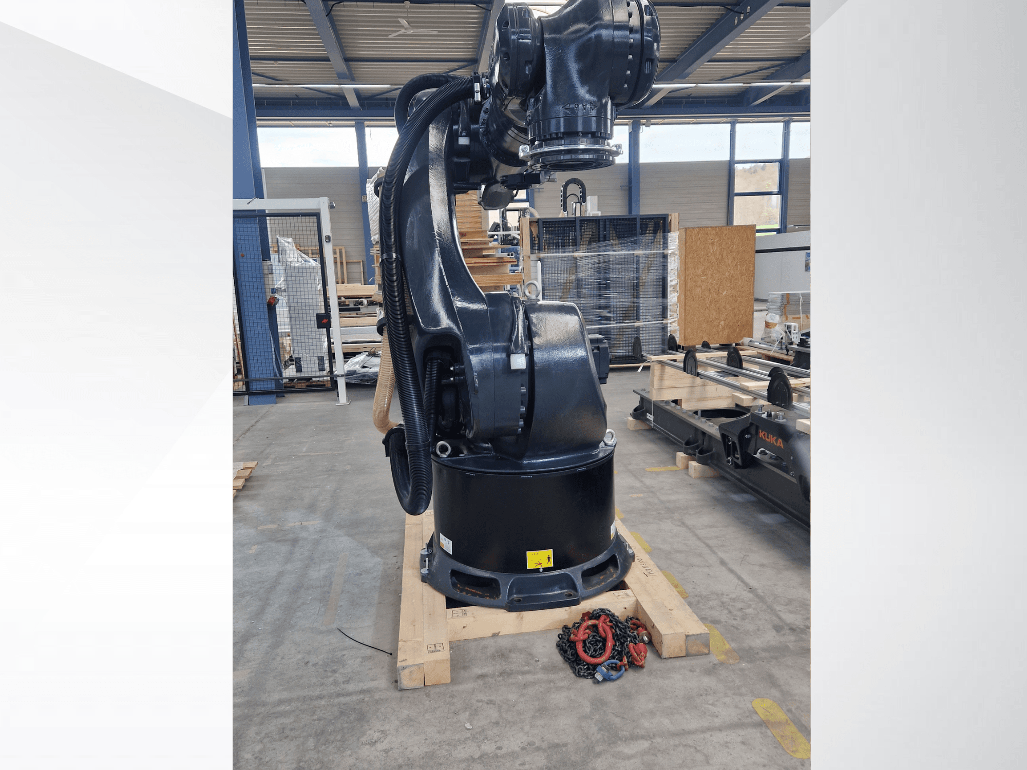 Robotska ruka KUKA KR 340 R3330 u skladištu, bočni pogled koji prikazuje njezinu bazu i kabele, s lancima u prvom planu.