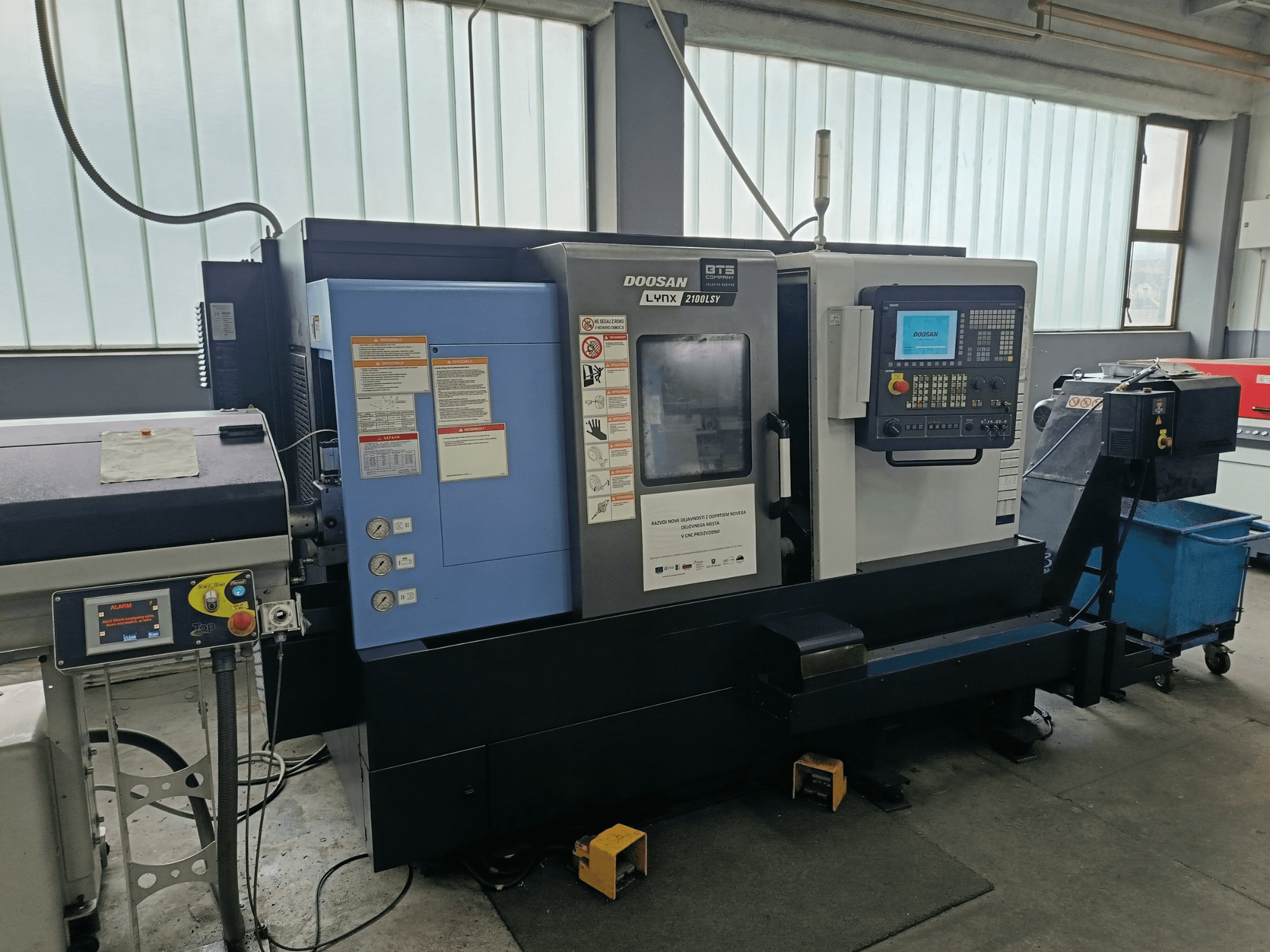 DOOSAN LYNX 2100 LSY Tokarsko-glodački centar, bočni pogled s upravljačkom pločom i operativnim gumbima, s vidljivim informativnim naljepnicama.