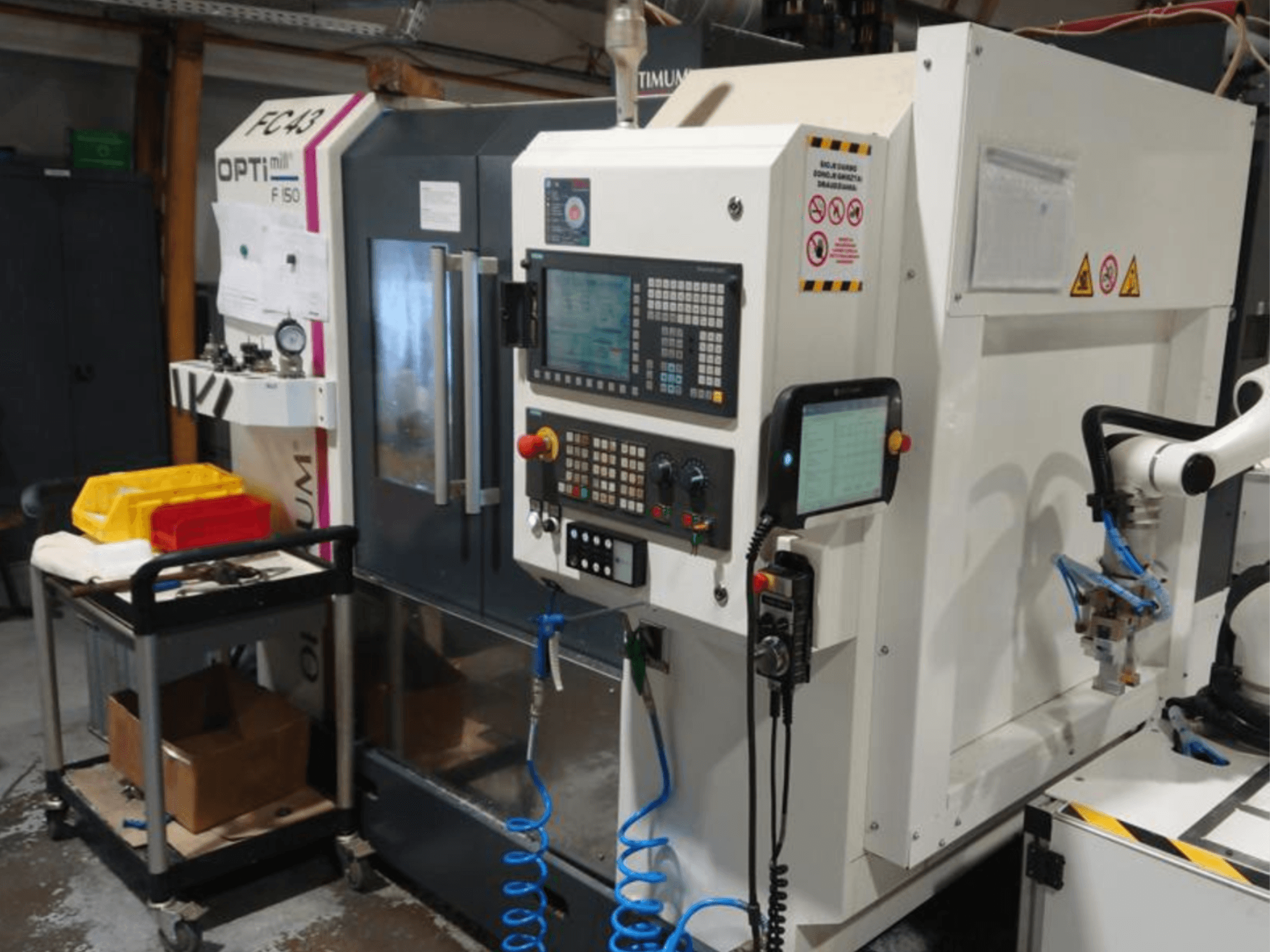 Upravljačka ploča glodalice OPTIMUM F50 s crijevima, alatima i robotskom rukom vidljivom u radioničkom okruženju.