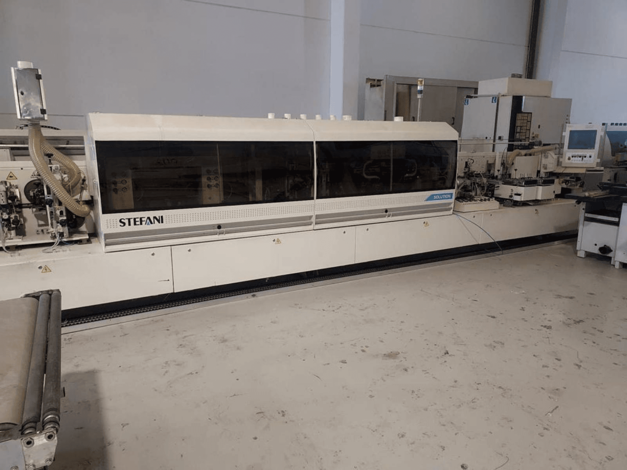 Stroj za lijepljenje rubova Stefani Solutions, pogled sprijeda, s vidljivim sustavom za usisavanje prašine i upravljačkom pločom, u radioničkom okruženju.