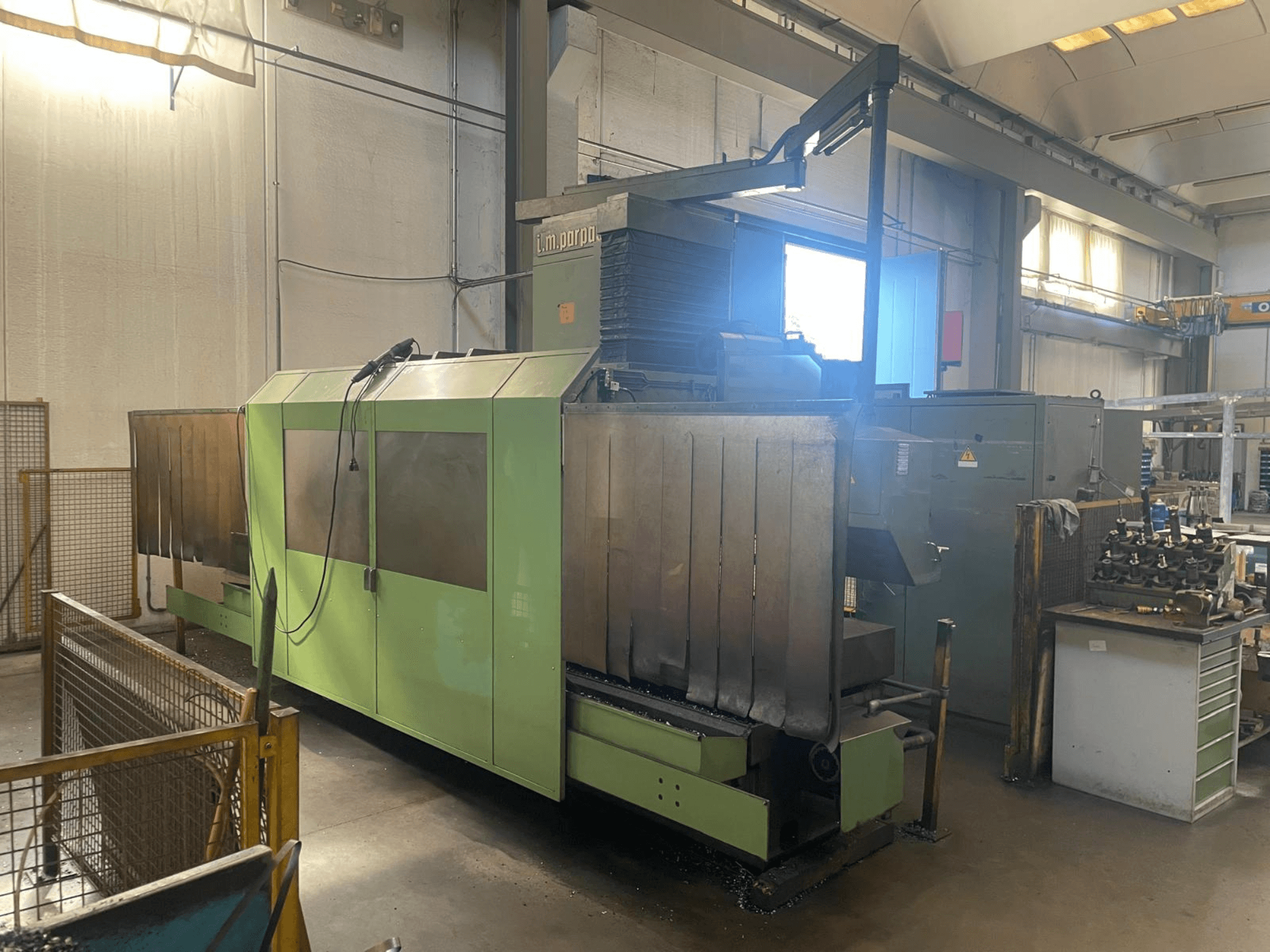 Zeleni industrijski stroj s vidljivim metalnim komponentama, prednji pogled; sadrži upravljačku ploču, sigurnosna upozorenja i radnu stanicu u blizini.