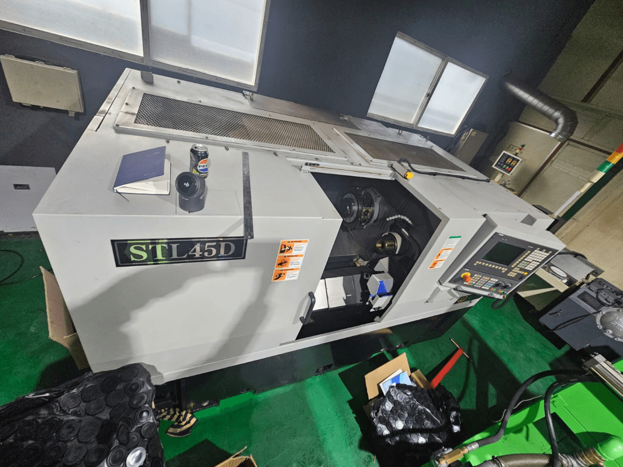 STL45D CNC stroj pogled odozgo, s prikazom upravljačke ploče, cilindričnog dijela, bilježnice i limenke na vrhu.