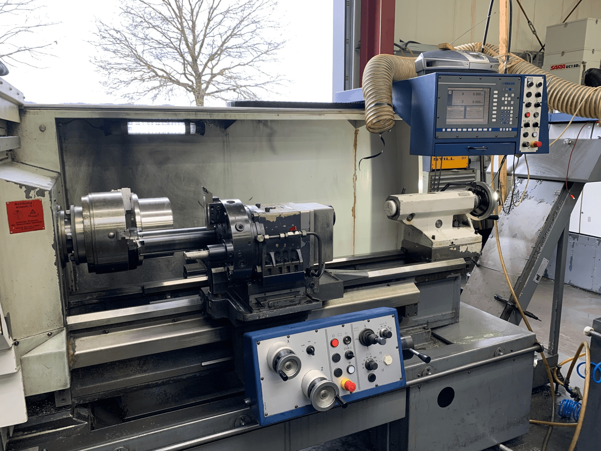 Weiler E55X1000 horizontalni tokarski stroj u radionici, s prikazom upravljačke ploče, tokarskog stroja i držača alata. Pogled sprijeda.