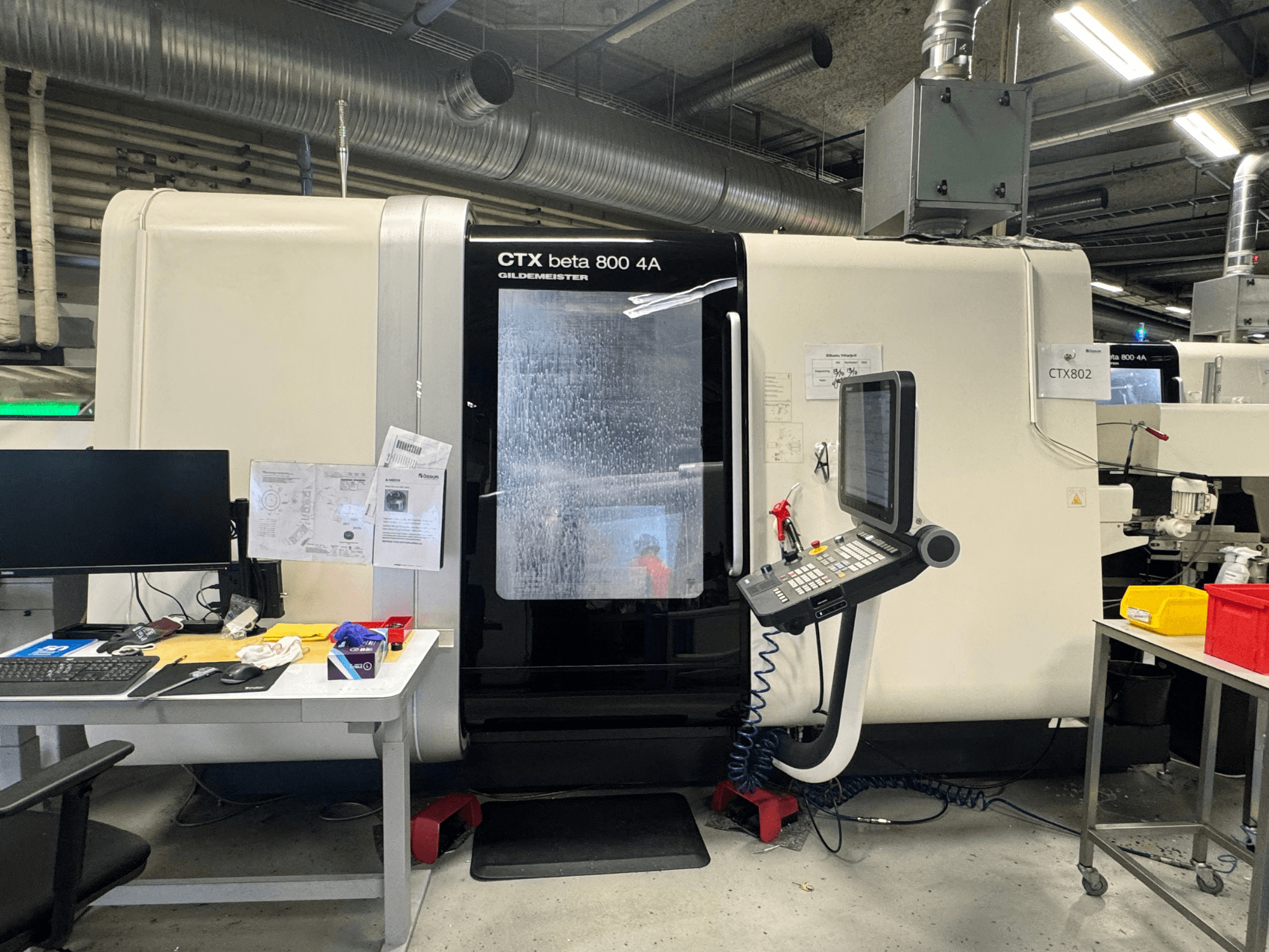 CNC stroj CTX beta 800 4A u radionici, bočni pogled koji prikazuje upravljačku ploču i radni prostor pretrpan alatima i dokumentima.