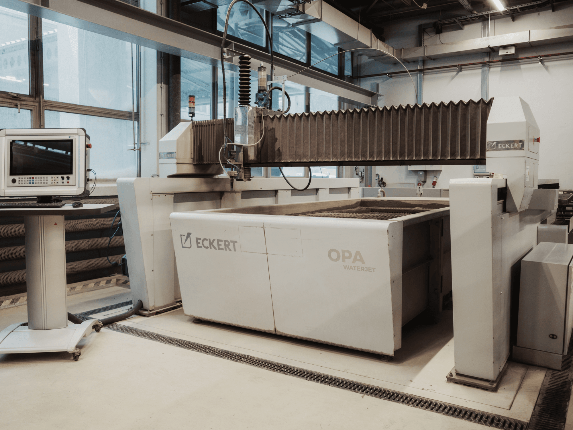 Stroj za rezanje ECKERT OPAL WATERJET-om u radionici, prikazan s prednje strane s upravljačkom konzolom u blizini.