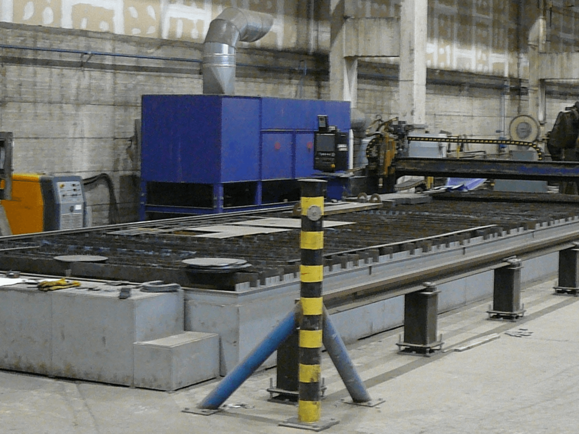 Industrijski stroj za rezanje metala, bočni pogled, s plavom upravljačkom kutijom, sigurnosnim prugama i metalnom radnom površinom.
