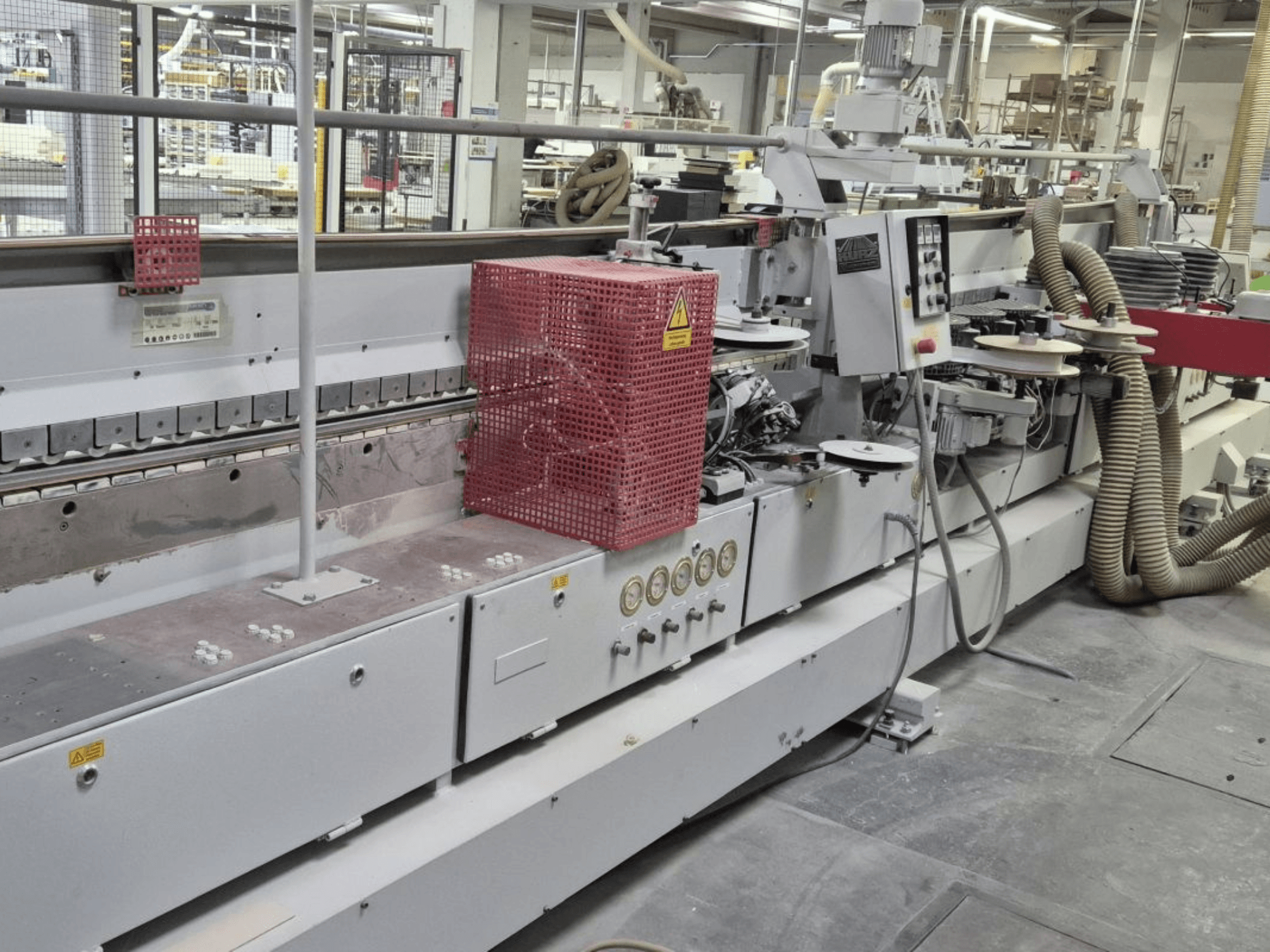 Stroj za obradu rubova s upravljačkom pločom, usisnim crijevima i crvenim sigurnosnim poklopcem, gledano iz bočnog kuta.