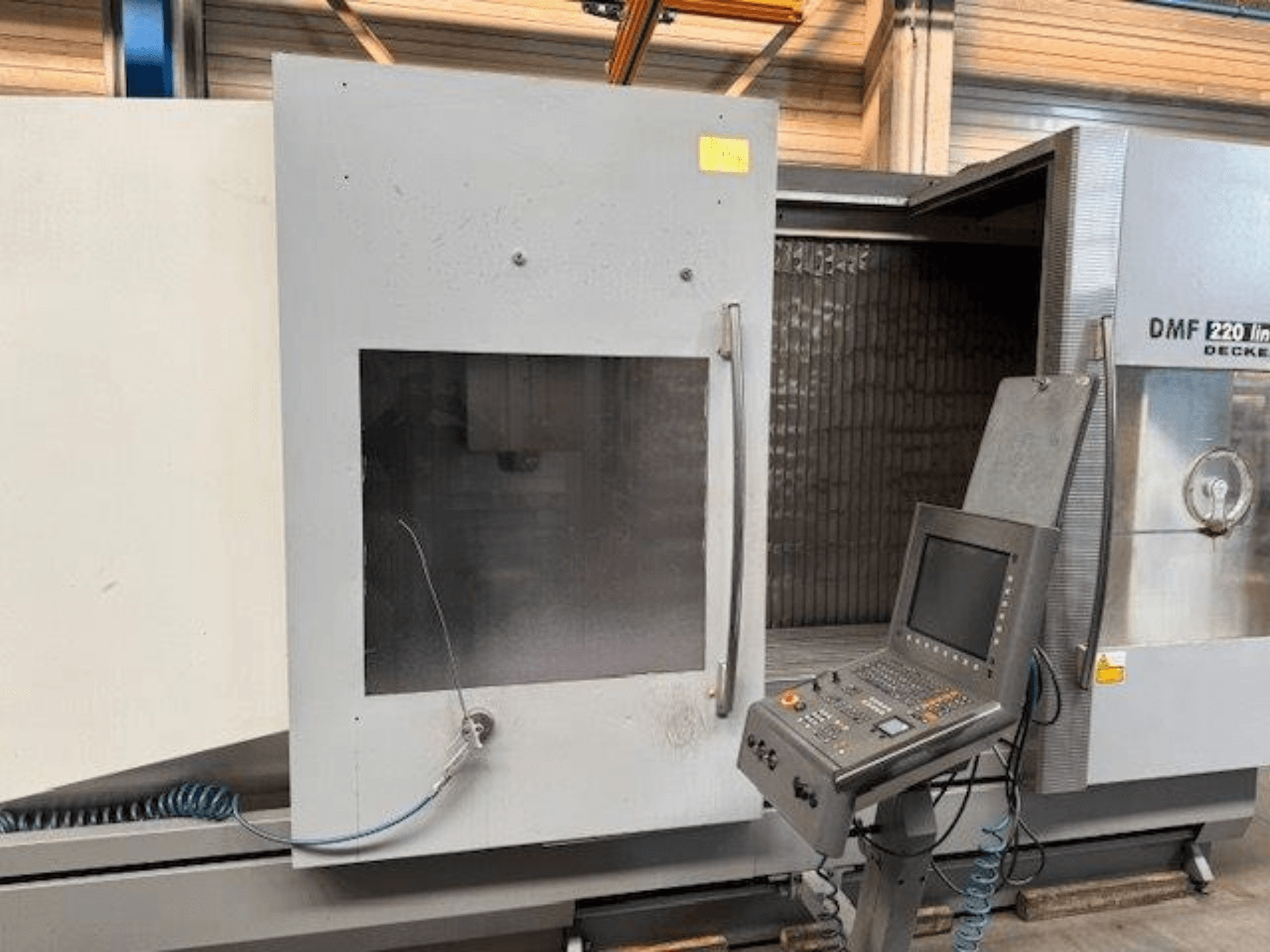 Prednji pogled na linearni vertikalni obradni centar DECKEL MAHO DMF 220, s prikazom upravljačke ploče i otvorenih vrata stroja.