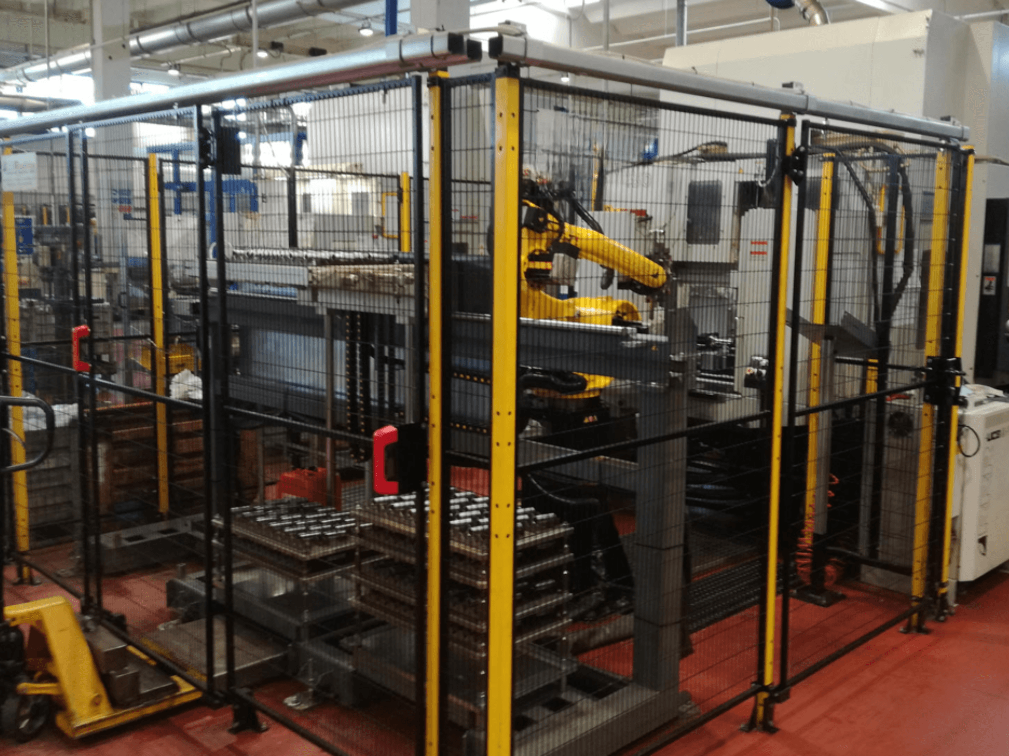 Vertikalni obradni centar Enshu EV450 u ograđenom radnom prostoru, s robotskim rukama i više naslaganih obradaka. Pogled sprijeda.