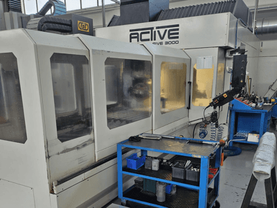 Aktivni CNC stroj 3000 u radionici, prednji pogled s alatima na plavim kolicima, vidljive kontrole i radni prostor unutra.