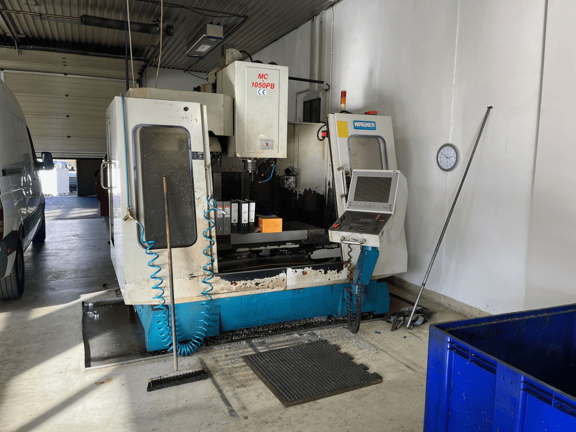 WAGNER MC 1050PB CNC stroj u radionici, pogled sprijeda, s upravljačkom pločom i radnim prostorom; vidljivo plavo crijevo za zrak i alati za čišćenje.