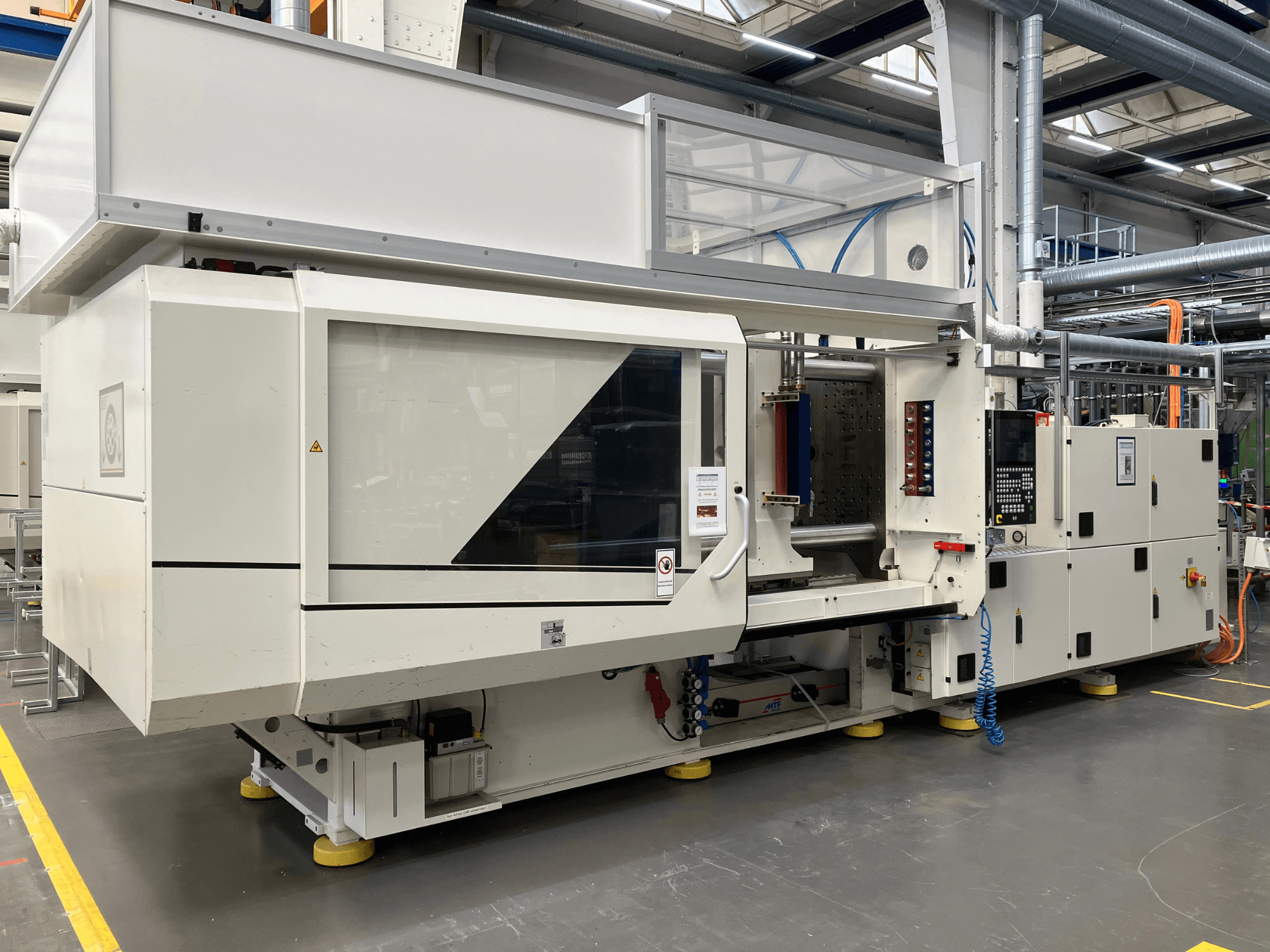 Bočni pogled na stroj za brizganje plastike, model AET, s upravljačkom pločom i prozirnim poklopcima, u industrijskom okruženju.