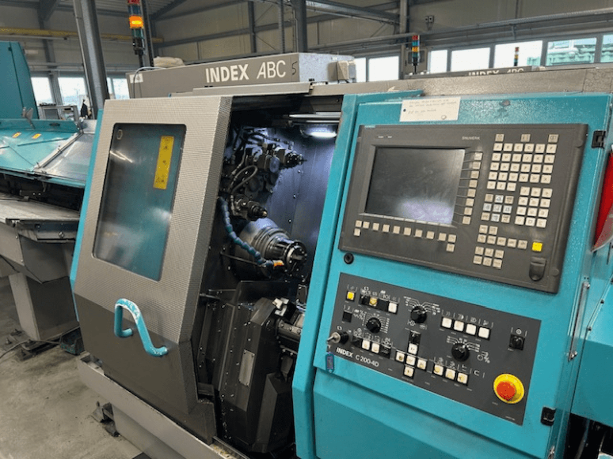 Prednji pogled na CNC tokarilicu INDEX C200-AD s upravljačkom pločom, vidljivim unutarnjim komponentama i sigurnosnim značajkama.