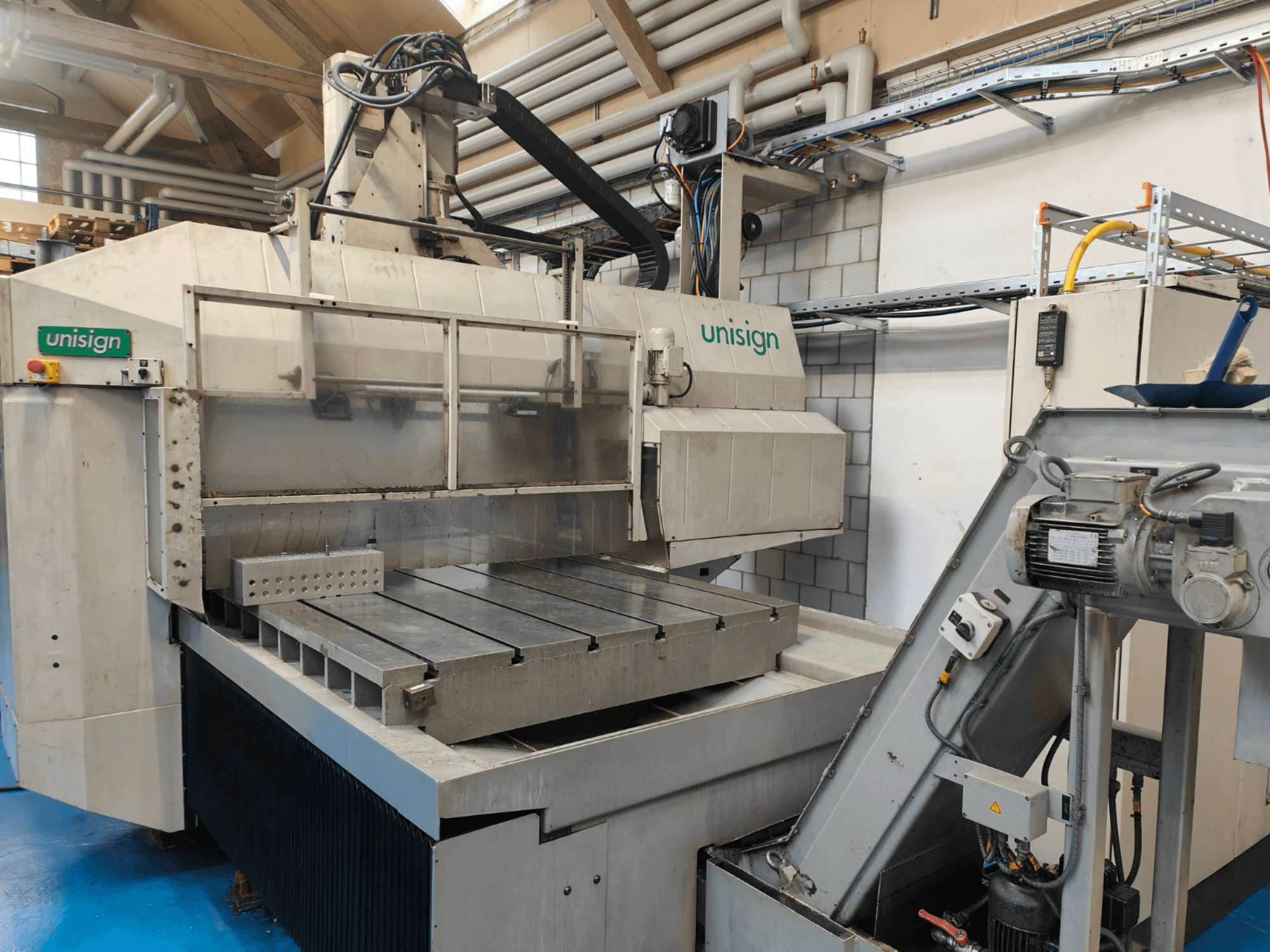 Unisign CNC stroj u radionici, prednji pogled, s velikim stolom, upravljačkom pločom i elementima industrijskog dizajna.