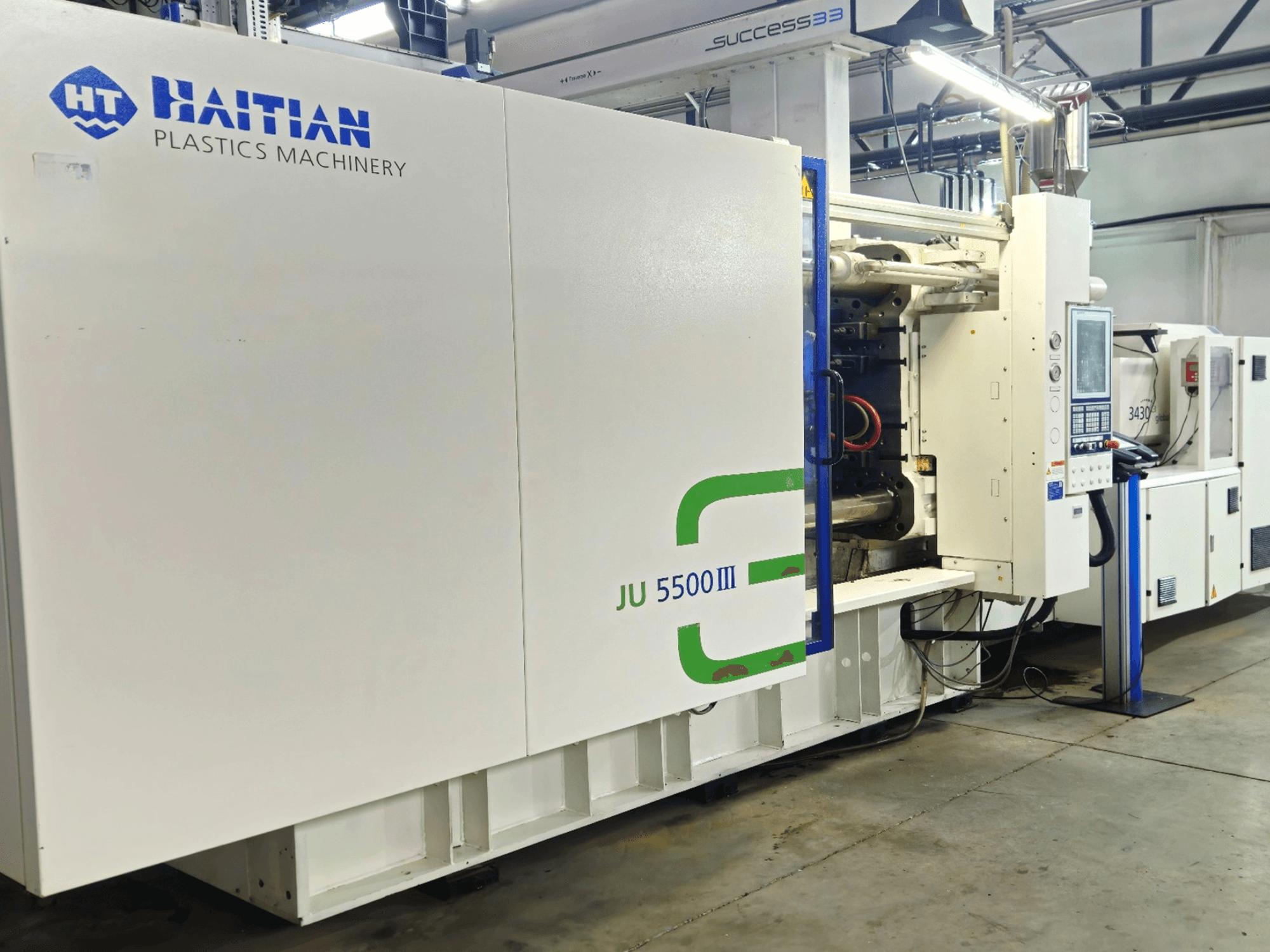 Haićanski stroj za plastiku JU 5500III u tvorničkom okruženju, prednji pogled s upravljačkom pločom i proizvodnim prostorom.