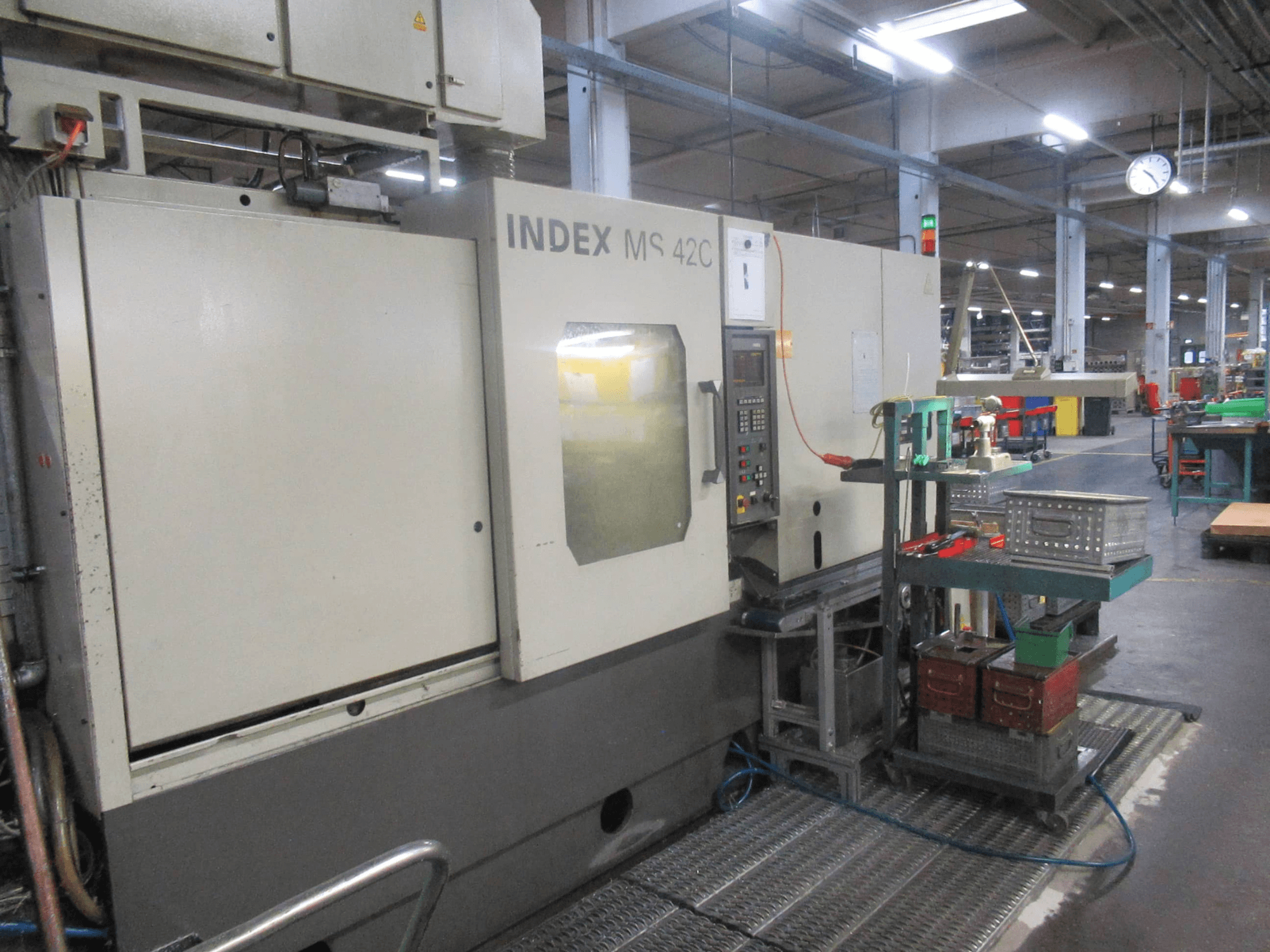 INDEX MS 42C CNC stroj u radionici, bočni pogled koji prikazuje upravljačku ploču i spremište alata na kolicima s kotačima.
