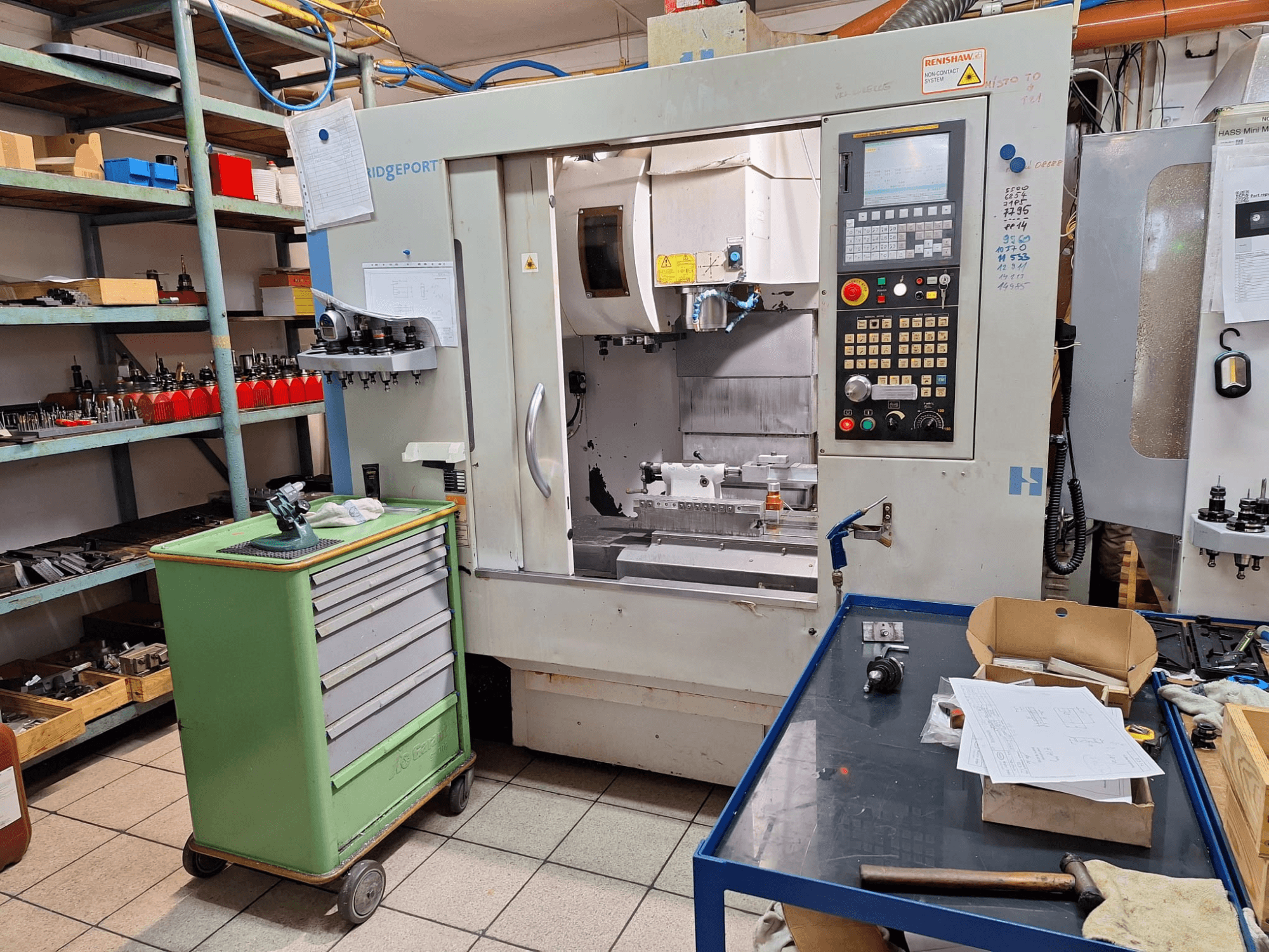Prednji pogled na vertikalni obradni centar Hardinge Bridgeport GX 710 s upravljačkom pločom, alatima i policama u radioničkom okruženju.
