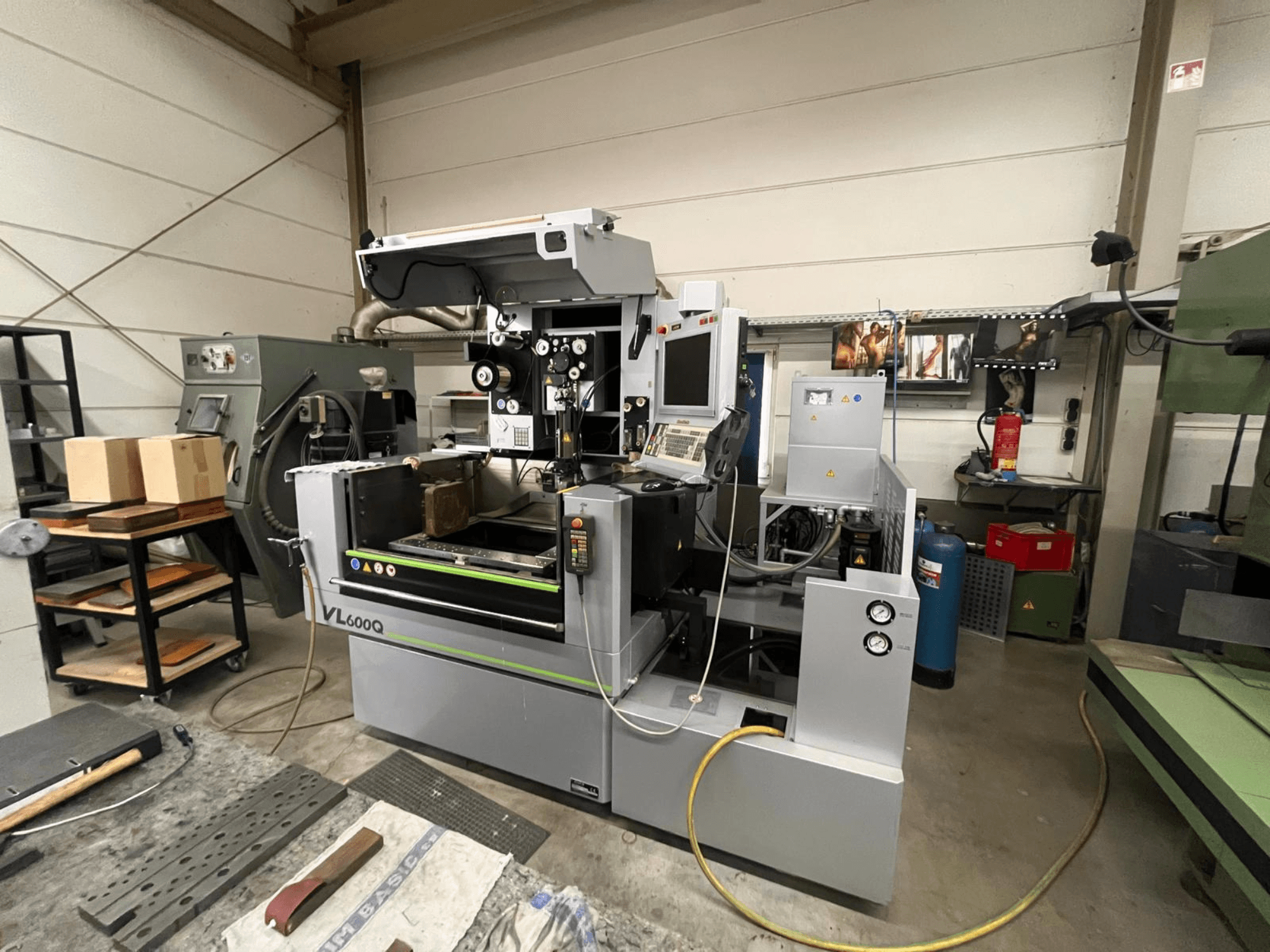 CNC stroj VL600Q u radionici, prednji pogled, s upravljačkom pločom, materijalom na mjestu i raznim alatima u blizini.