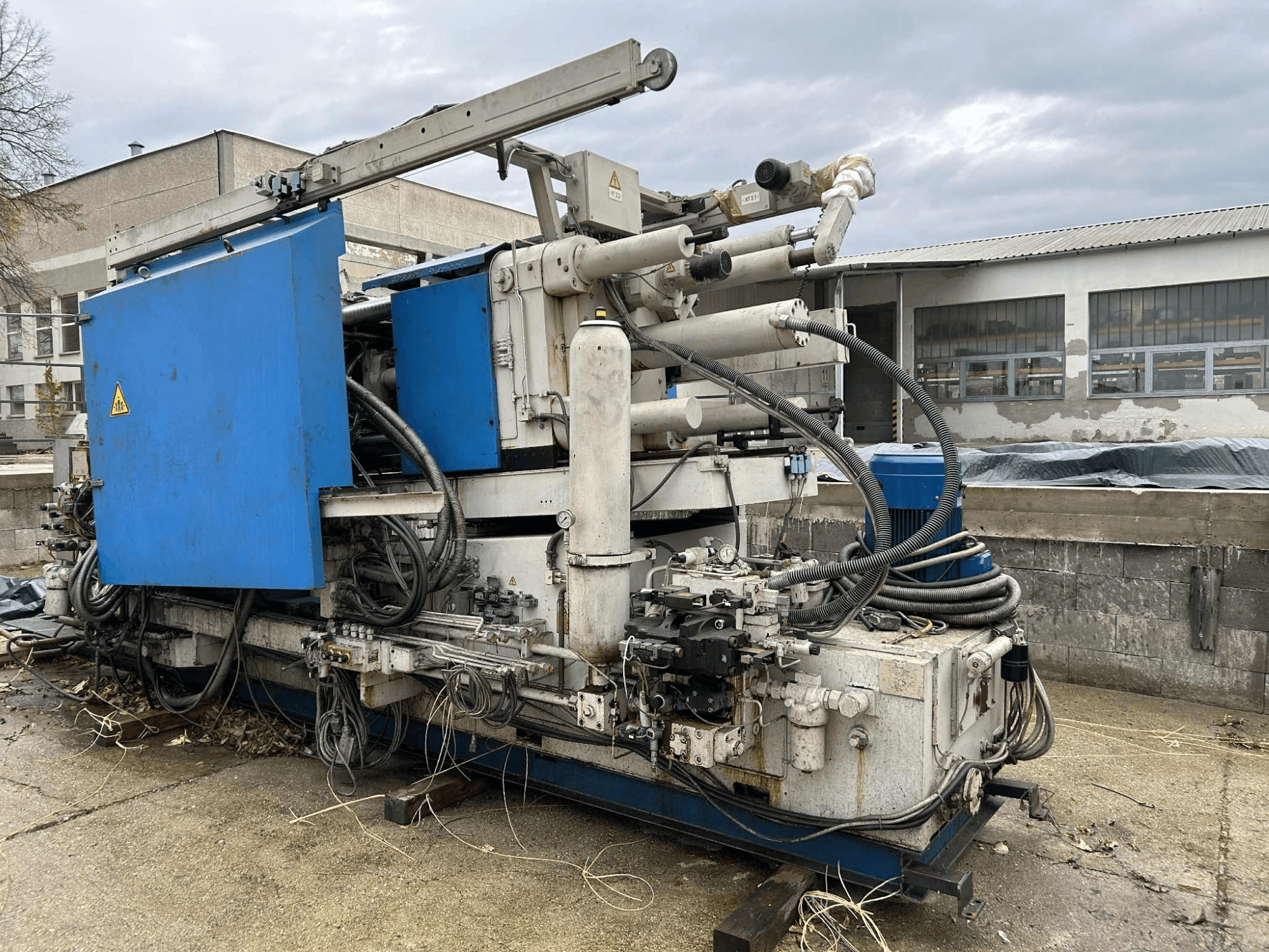 Veliki industrijski hidraulički stroj s plavim kućištem, raznim crijevima i metalnim komponentama, gledano sa strane.