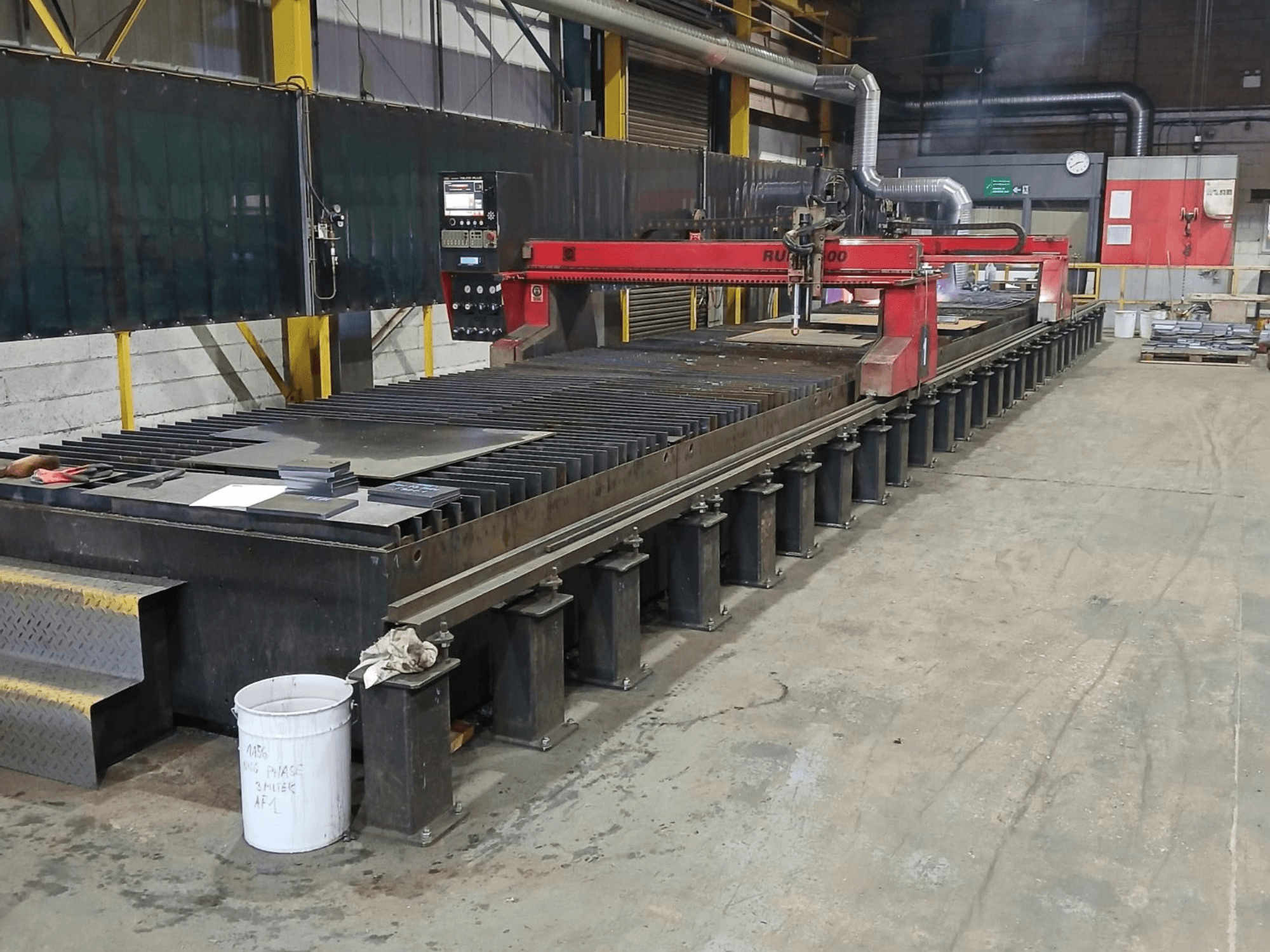 Crveni stroj za rezanje RUIDA 300, bočni pogled, s metalnim limom na čeličnom stolu, smješten u industrijskom radnom prostoru.