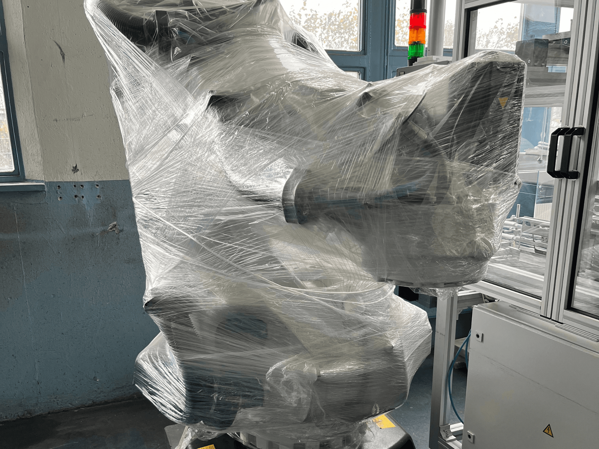 Industrijska robotska ruka omotana plastikom, prednji pogled. Uključuje upravljačku jedinicu i indikatorsku lampicu. Marka nije vidljiva.