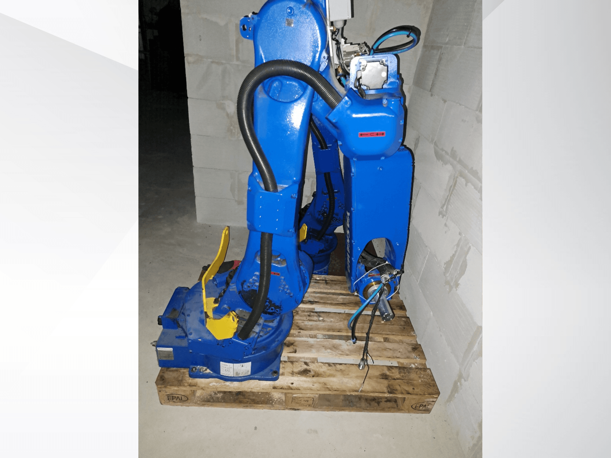 Robotska ruka Yaskawa Motoman GP25 u plavoj boji, bočni pogled na drvenoj paleti, s kabelima i mehaničkim spojevima.