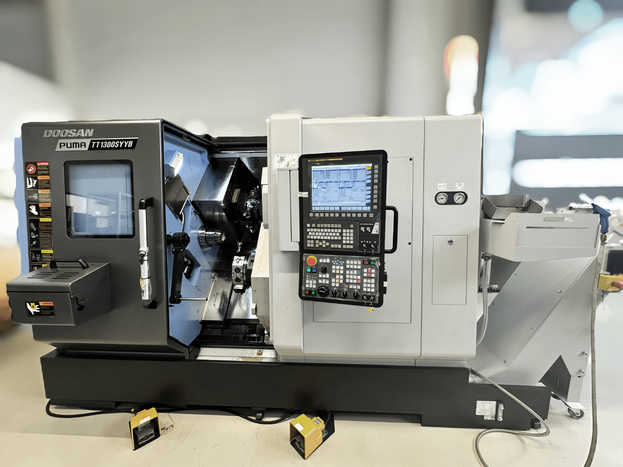 Bočni pogled na tokarsko-glodački centar Doosan Puma TT1300SYYB, s prikazom upravljačke ploče i unutrašnjosti stroja s vidljivim alatima.