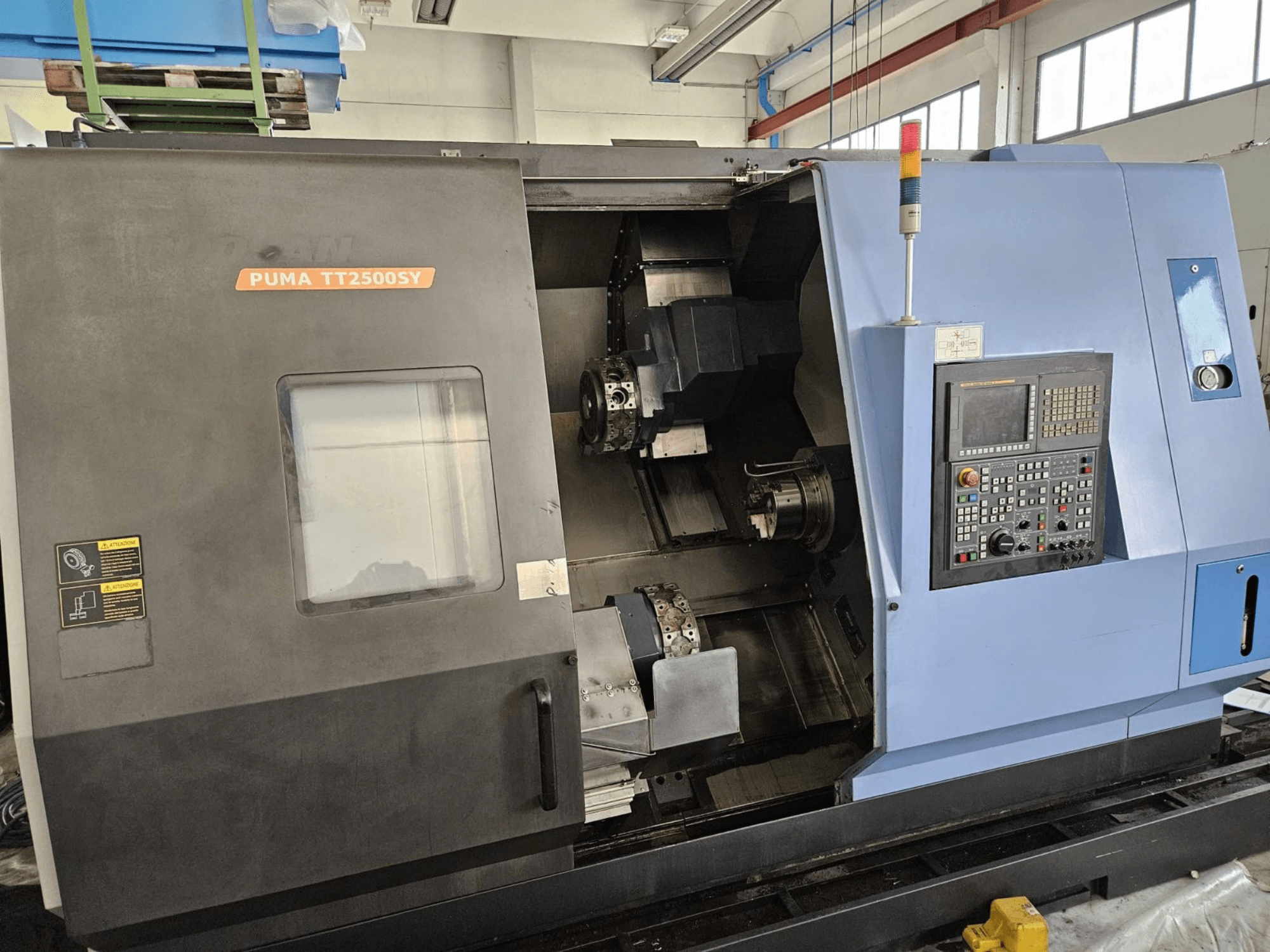 Viševretenski tokarski stroj DOOSAN PUMA TT2500SY, prednji pogled s prikazom upravljačke ploče i detalja unutrašnjosti stroja.