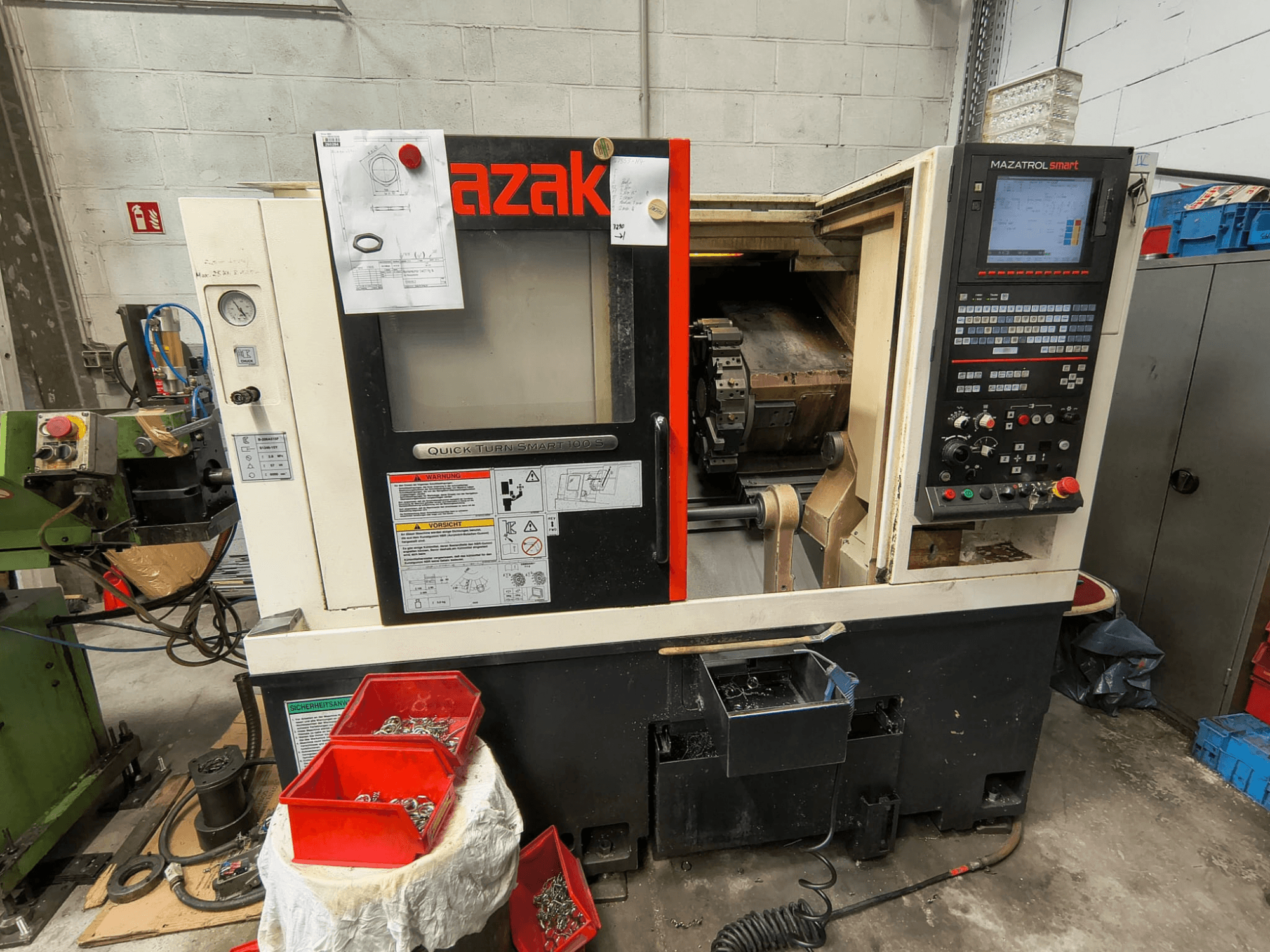 Mazak Quick Turn Smart 100 S, bočni pogled koji prikazuje upravljačku ploču, posudu za rashladnu tekućinu i spremnike s vijcima.