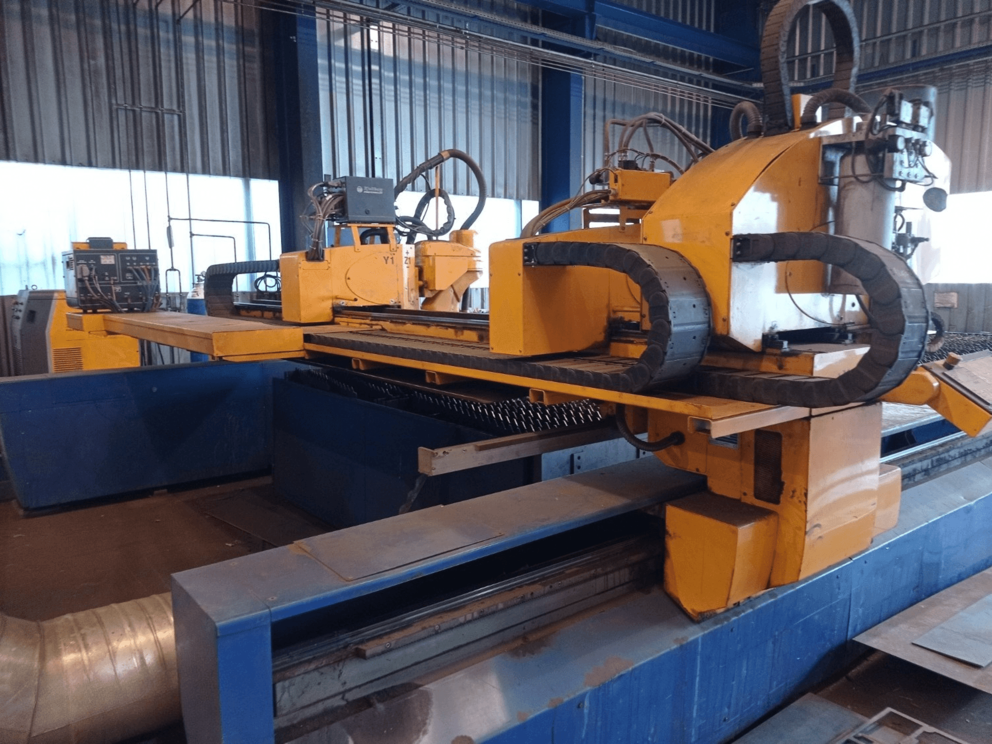 Žuti CNC stroj za plazma rezanje s dva horizontalna kraka, prikazan s prednje strane, s upravljačkom pločom i postoljem za rezanje.