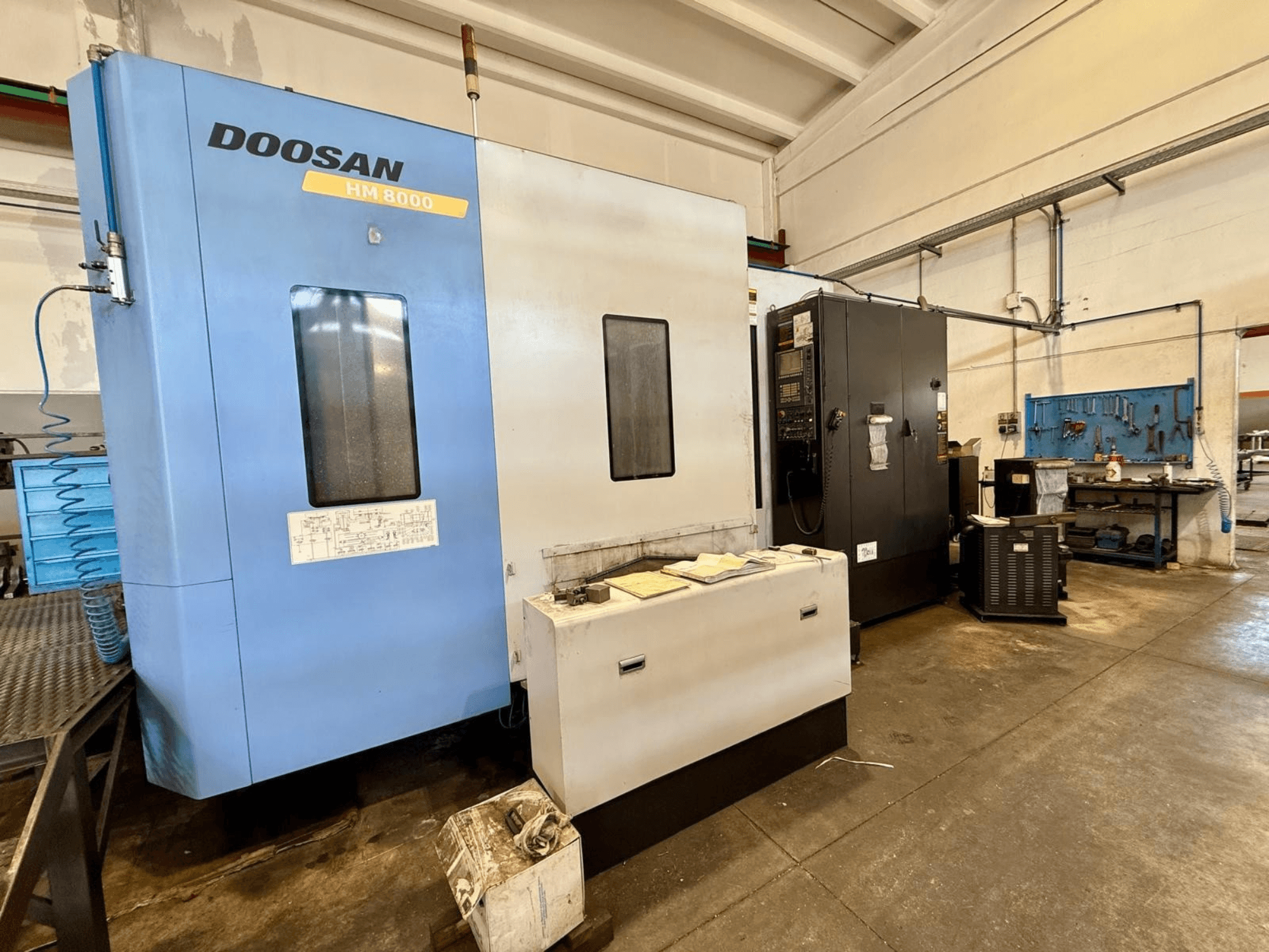 Horizontalni obradni centar DOOSAN HM 8000 u plavoj boji, prednji pogled, prikazuje upravljačku ploču i obližnju radioničku opremu.