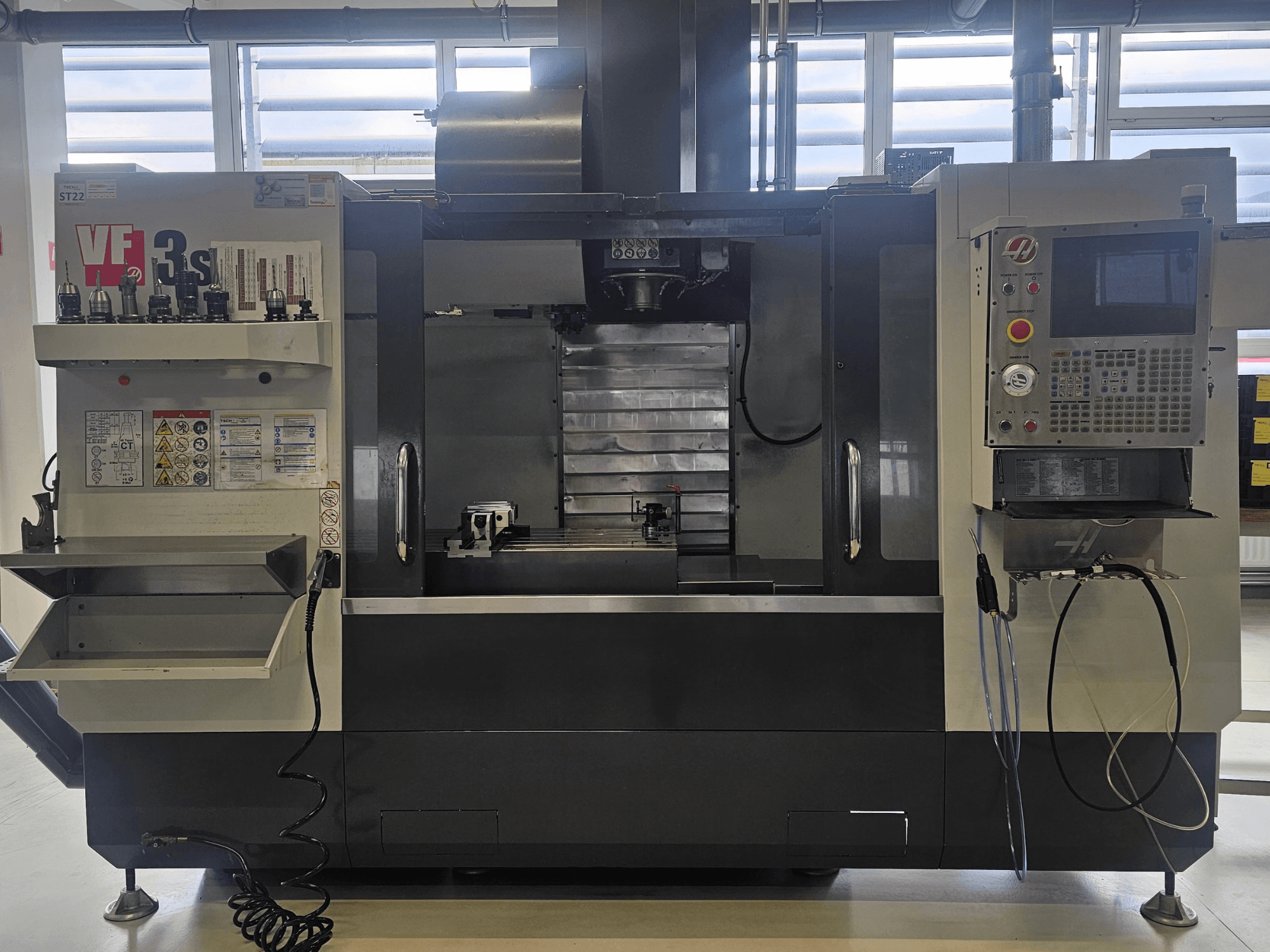 Haas VF3SS CNC glodalica, prednji pogled, s držačima alata, upravljačkom pločom i praznom posudom za rashladno sredstvo, s vidljivim sigurnosnim naljepnicama.