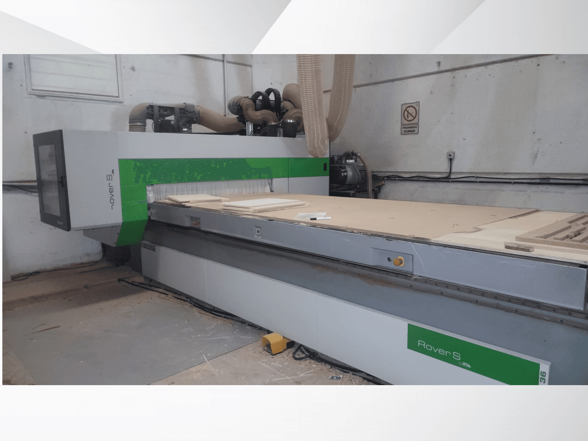 Prednji pogled na CNC stroj Biesse Rover S, s velikom radnom površinom s drvenim pločama i crijevima za usisavanje prašine.