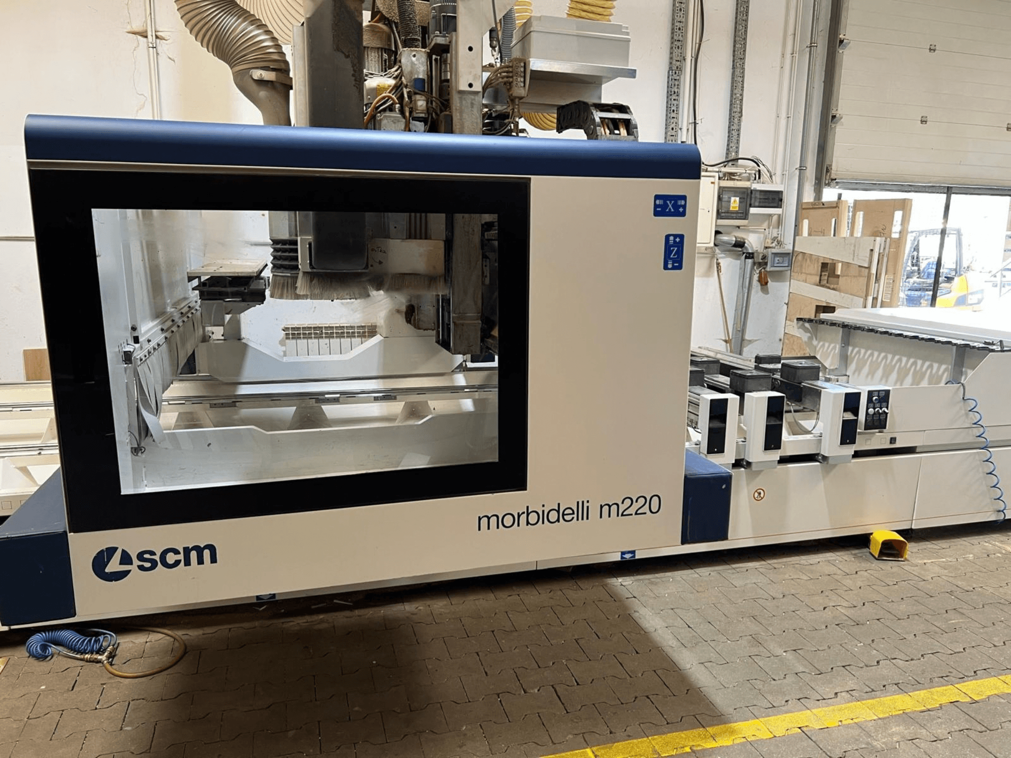 Prednji pogled na CNC obradni centar SCM Morbidelli M220, s velikim prozorom, upravljačkom pločom i radnim prostorom.