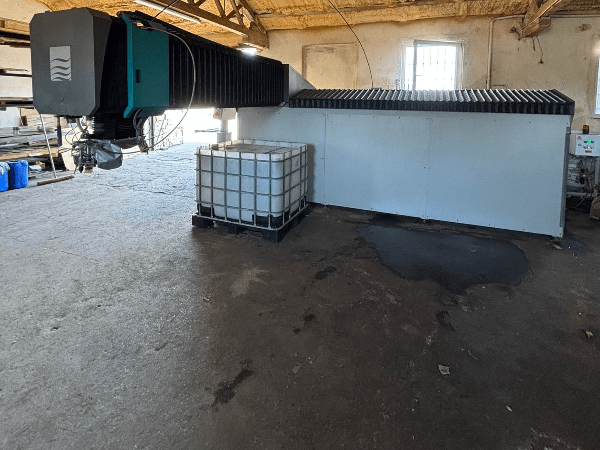 Industrijski stroj za vodeni mlaz u radionici, bočni pogled, s velikim spremnikom vode i upravljačkom pločom vidljivom pored njega.