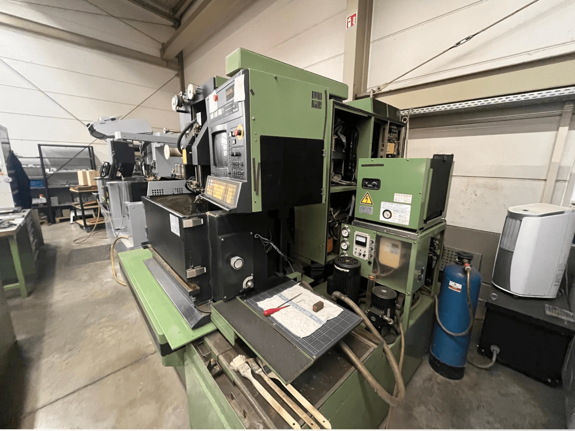 Zeleni industrijski stroj s upravljačkom pločom, bočni pogled; uključuje hidraulične komponente i radnu površinu s alatima.