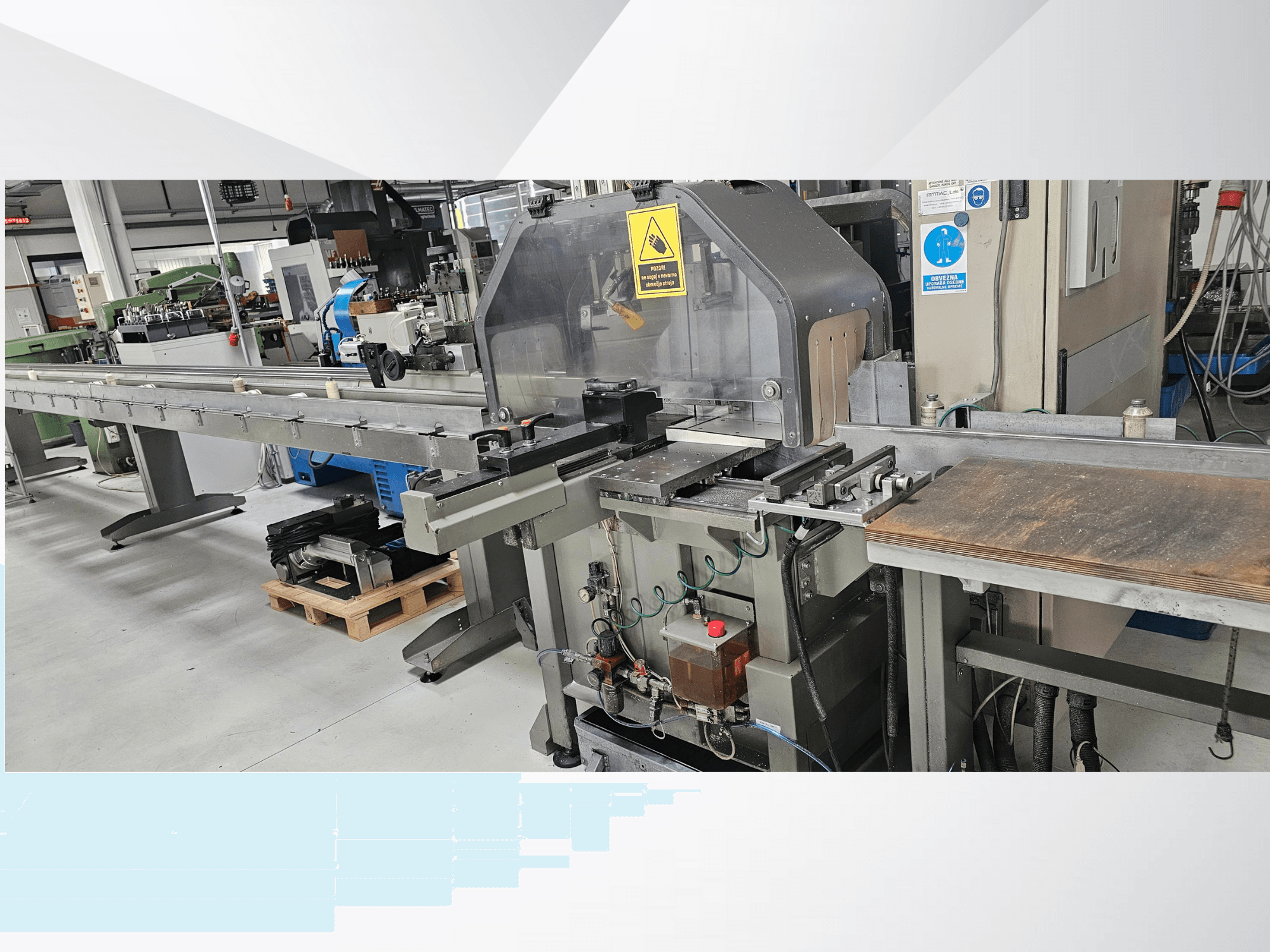 Industrijski stroj za rezanje iz bočnog pogleda, s dugim transporterom, upravljačkom pločom i sigurnosnim upozorenjima.