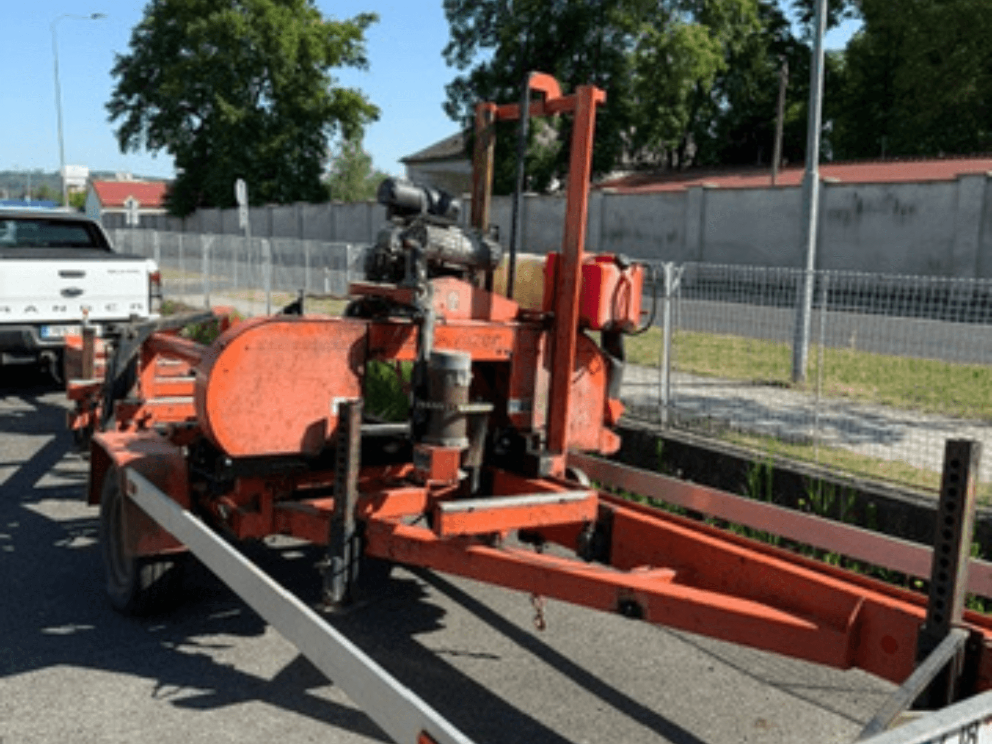 Tračna pila za drvo WOOD-MIZER LT40 u narančastoj boji, bočni pogled na prikolici s vidljivim kotačima i komponentama motora.
