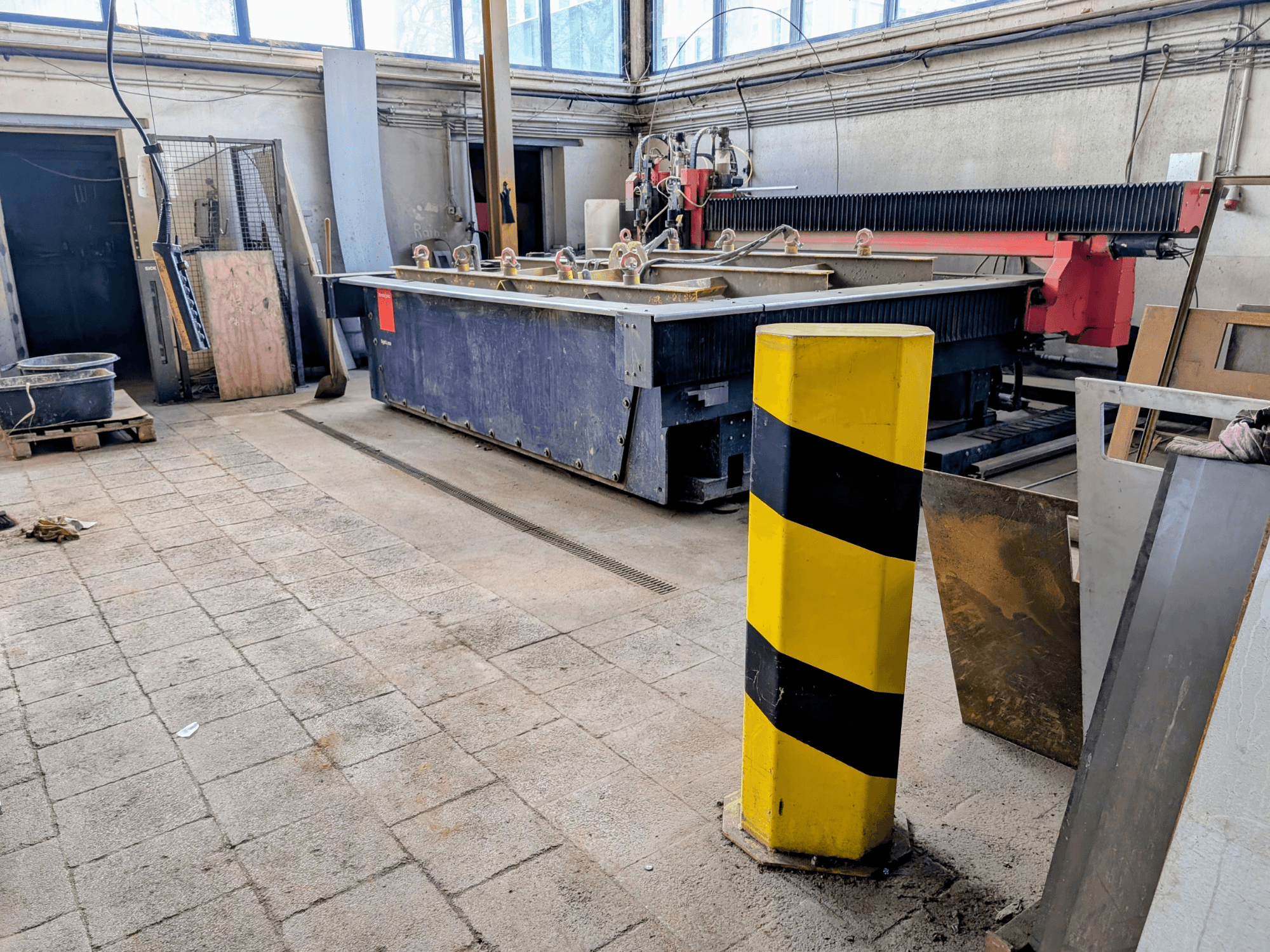 Stroj za rezanje vodenim mlazom Bystronic Byjet L 2030 u radionici, bočni pogled, sa žutim sigurnosnim stupom i okolnim materijalima.