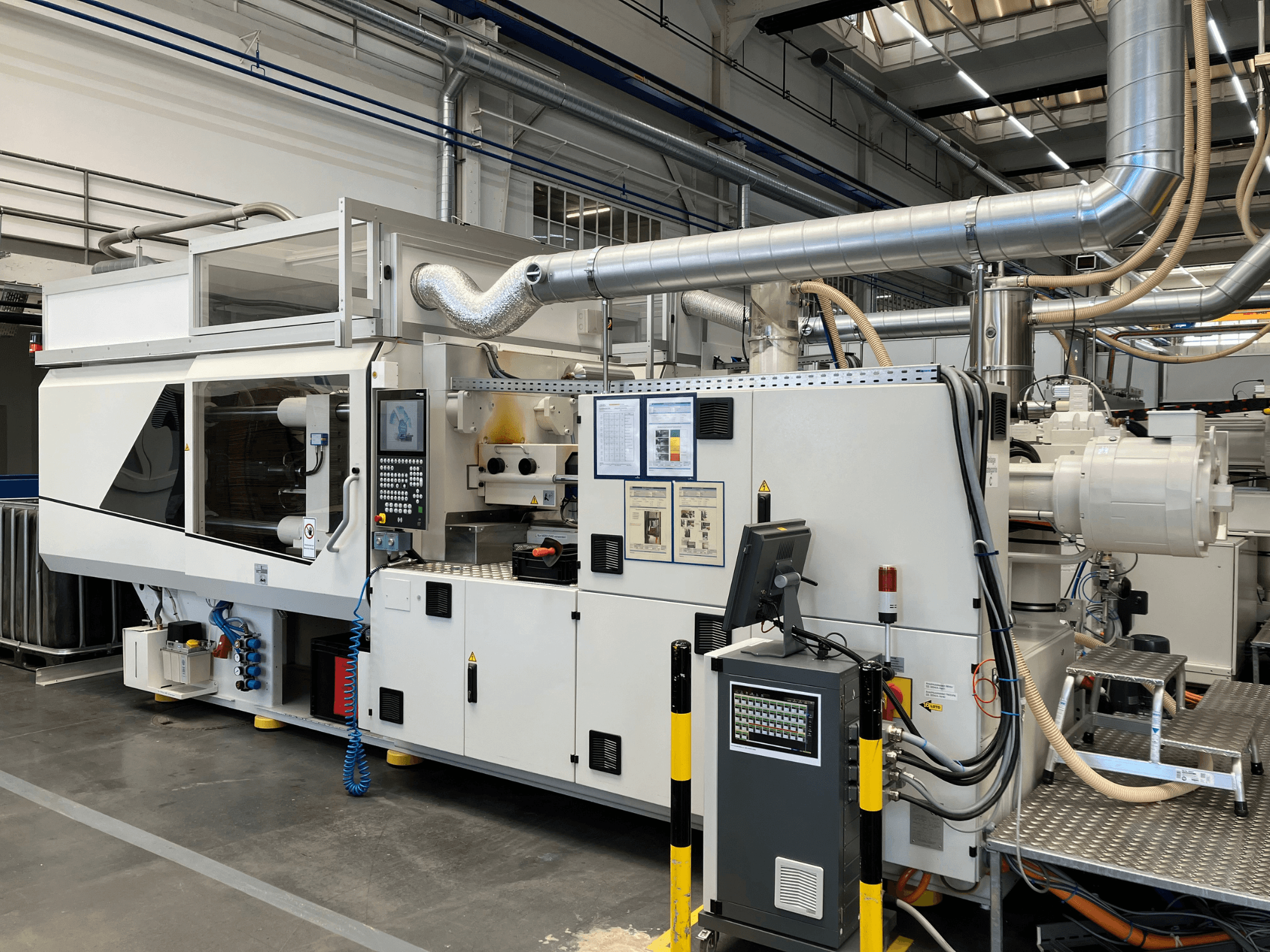 Prednji pogled na industrijski stroj s upravljačkom pločom, cijevima i zaslonima, s elegantnim bijelim dizajnom i tehničkim detaljima.