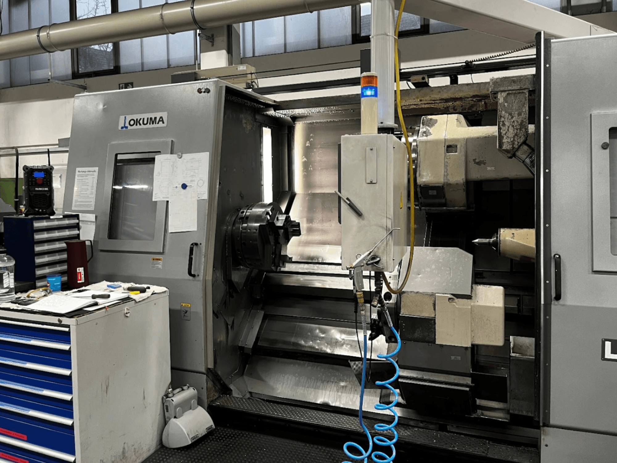 Okuma LU35-M horizontalni tokarski stroj, prednji pogled. Sadrži upravljačku ploču, alate i veliku steznu glavu za strojnu obradu.